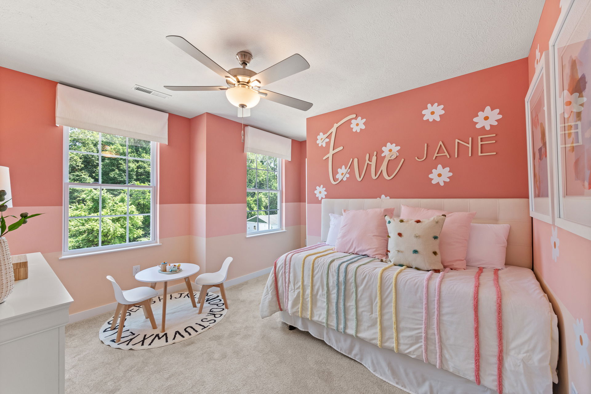A pink and white girl's bedroom featuring a bed with colorful striped bedding, a small table with chairs, and wall decor spelling 