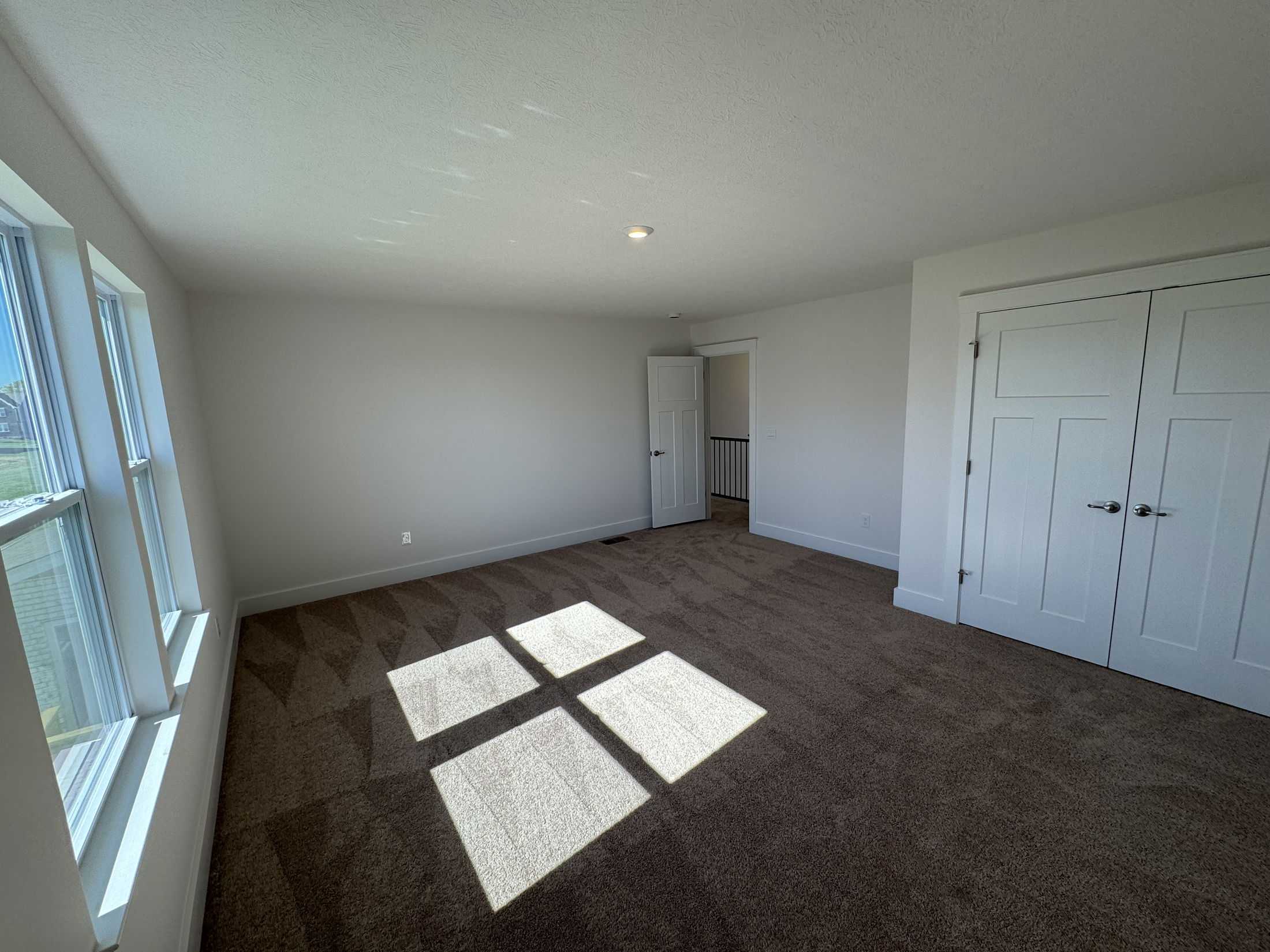 Spacious and bright empty room with large windows, neutral walls, and plush carpeting, ideal for personalization and decorating.