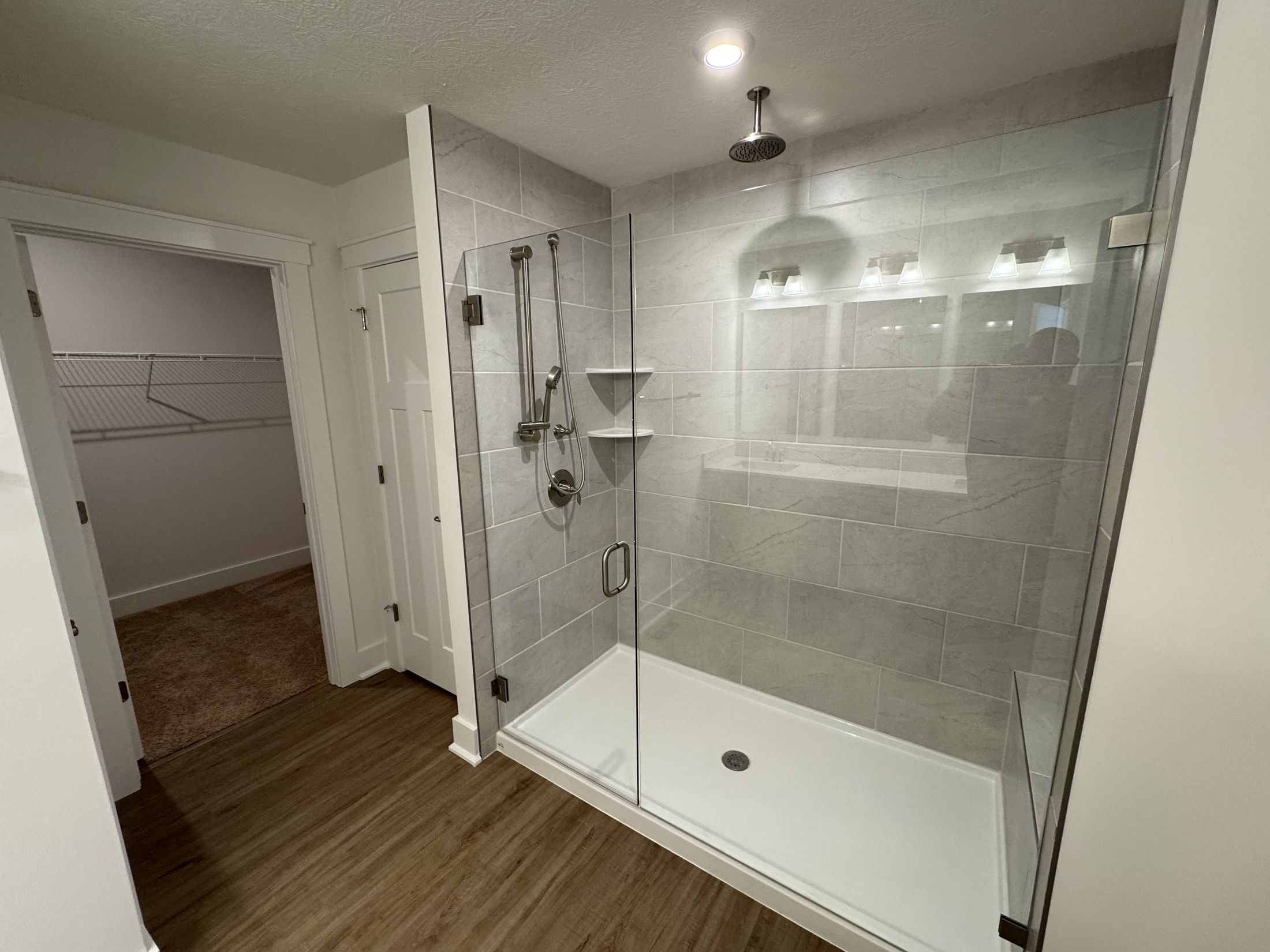 Modern bathroom featuring a glass shower enclosure, grey tiled walls, and a spacious layout.