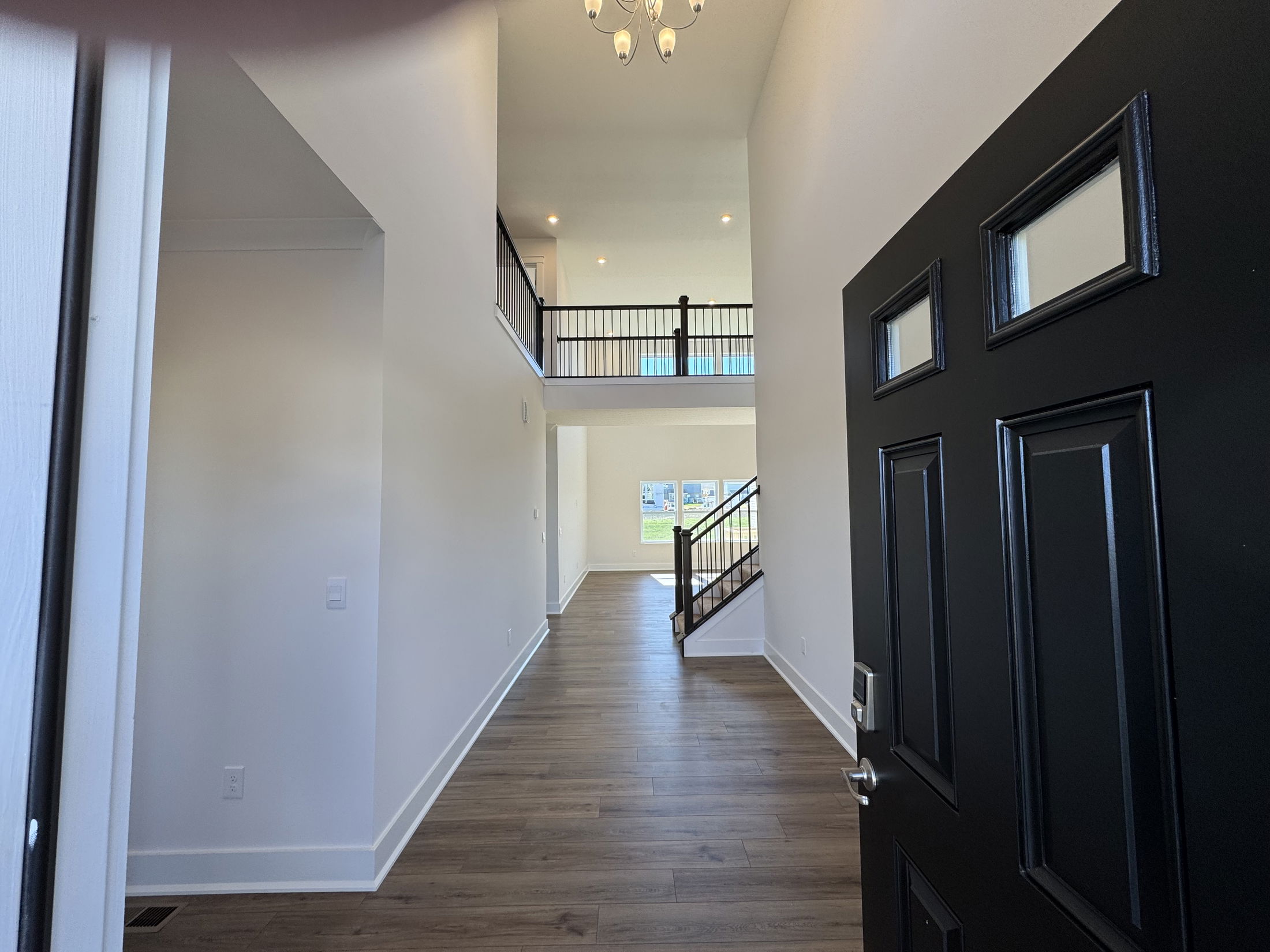Welcoming entryway view of a modern home featuring a black front door and a spacious foyer with hardwood flooring.