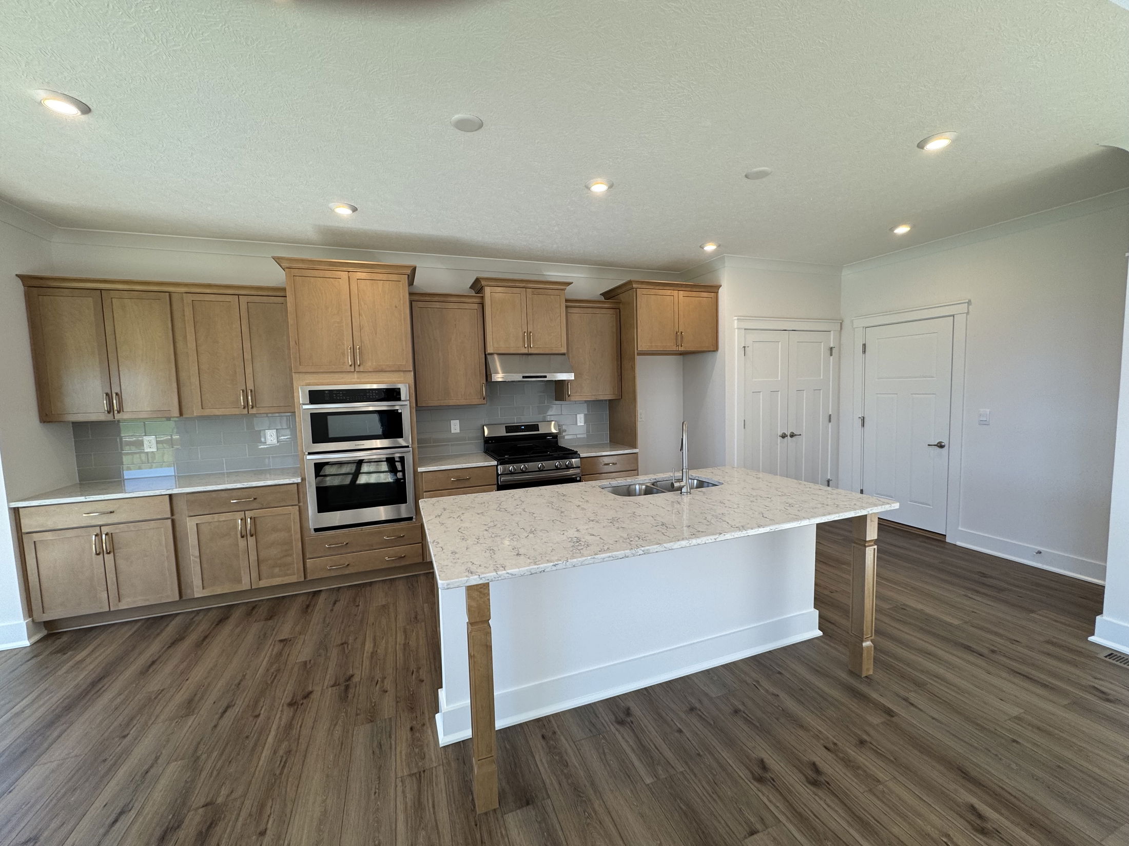 Modern kitchen interior featuring light wood cabinetry, stainless steel appliances, and a spacious island with a marble countertop.