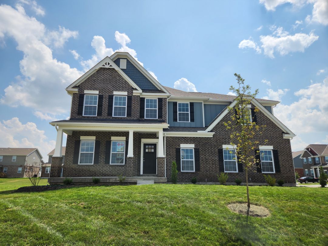 Two-story brick house with a gabled roof in a suburban neighborhood under a blue sky.
