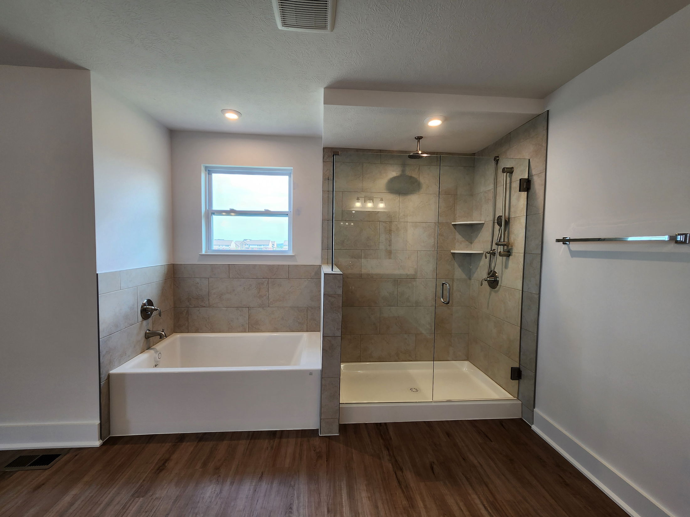 Modern bathroom with a glass-enclosed shower and separate bathtub featuring tile walls and wood-style flooring.