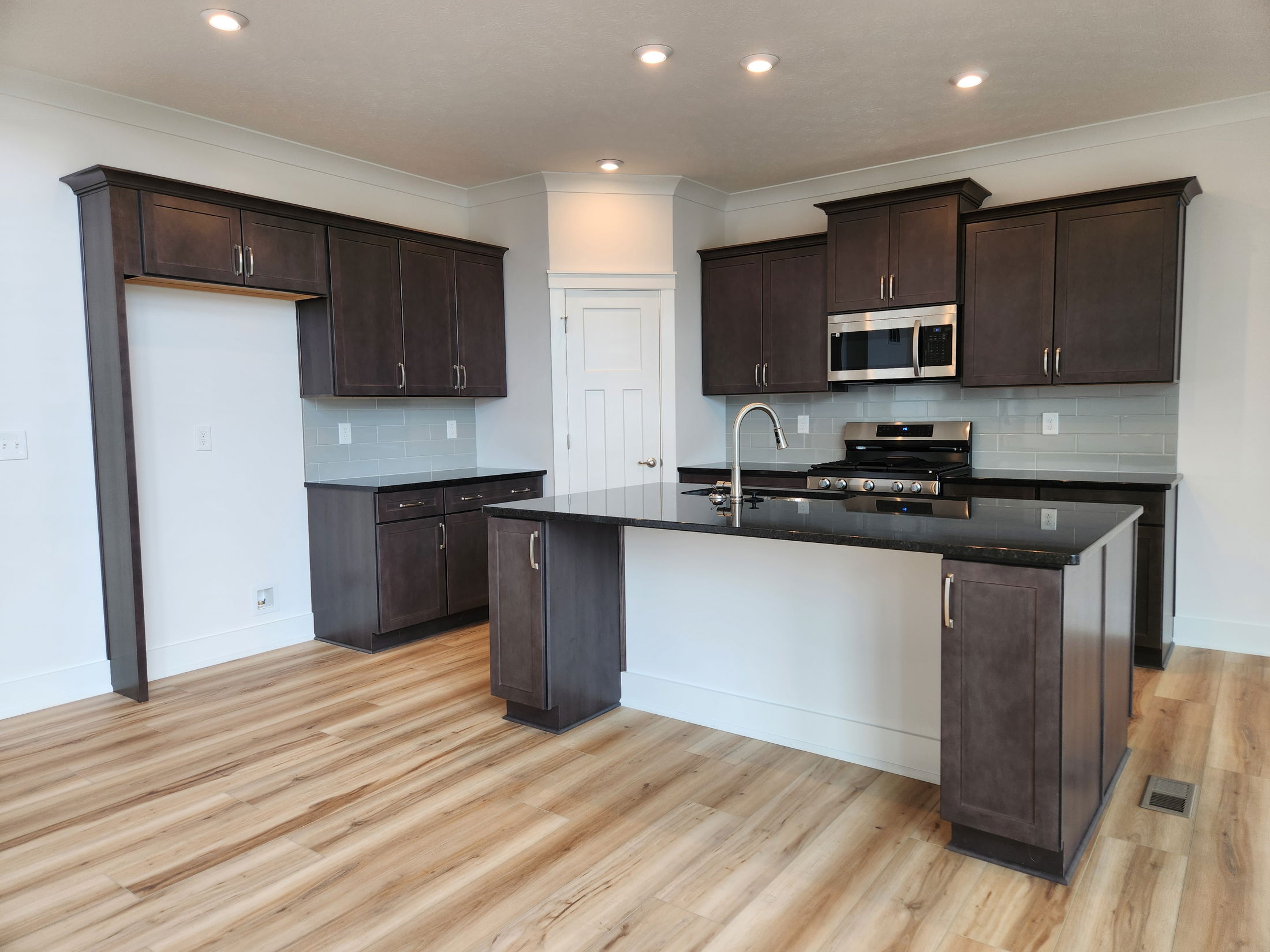 Modern kitchen with dark wood cabinets, stainless steel appliances, and a large island on light wooden floors.