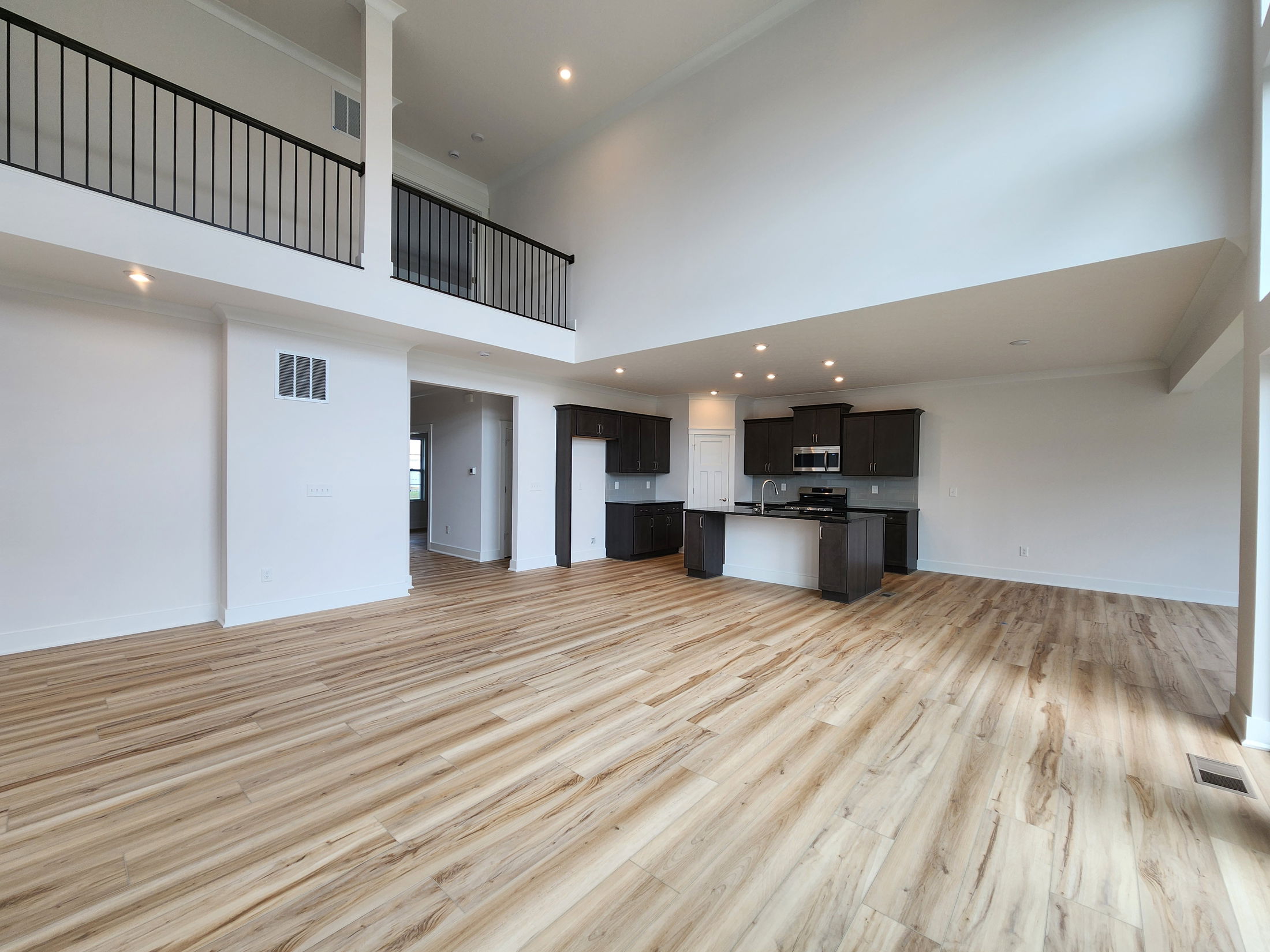 Spacious modern open-concept living area with high ceilings, dark wood kitchen cabinetry, and light wood flooring.