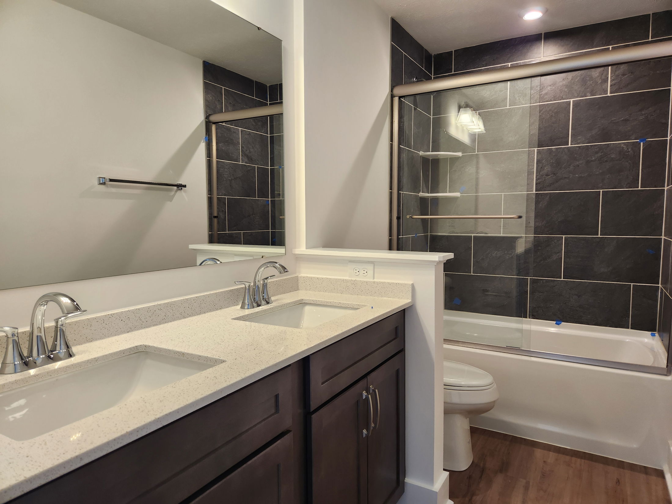 Modern bathroom with dark wood cabinetry, dual sinks with chrome faucets, and a tiled shower with glass doors.