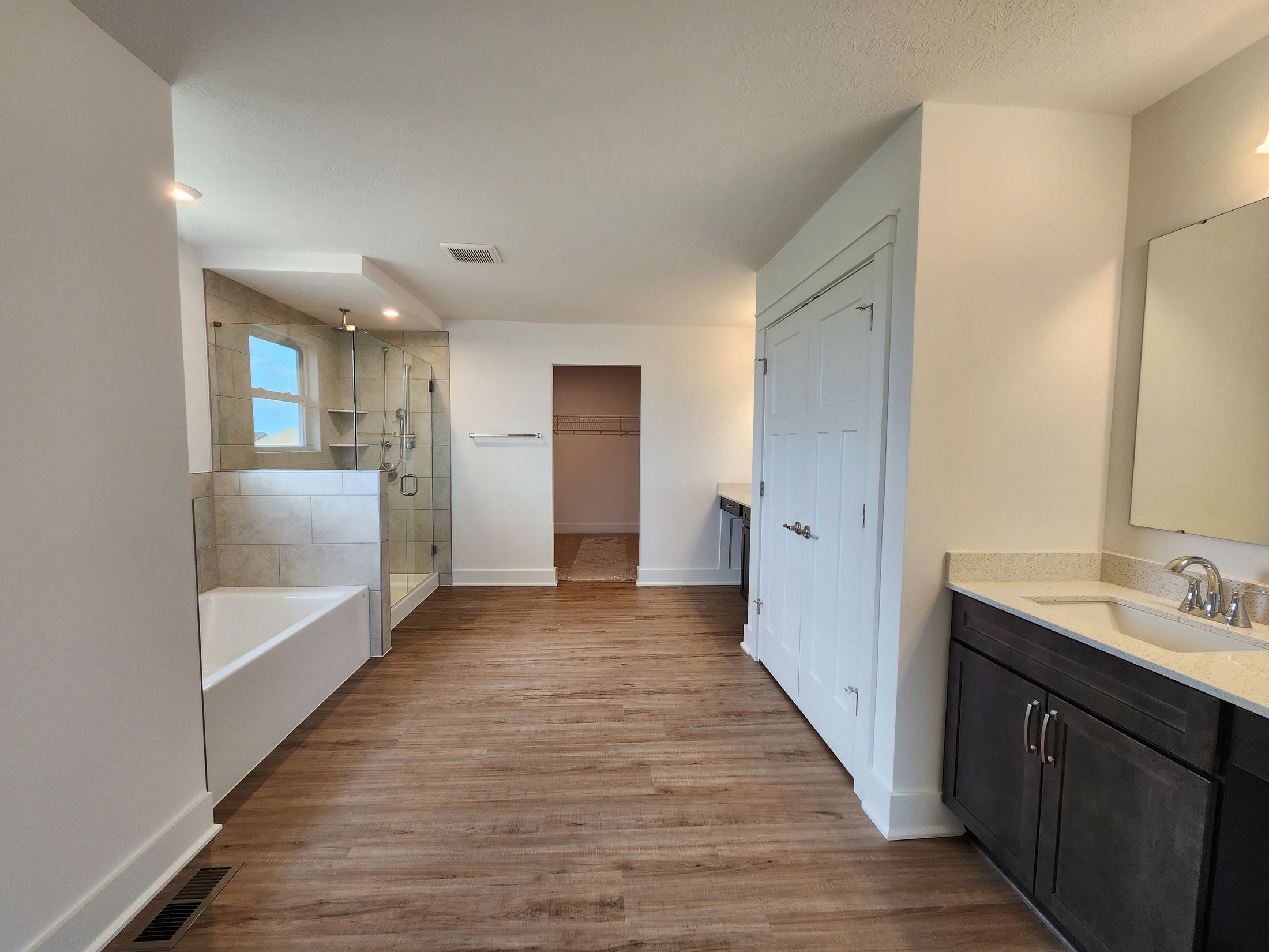 Modern bathroom with wood flooring, glass shower, and dark wood vanity with a wide mirror.