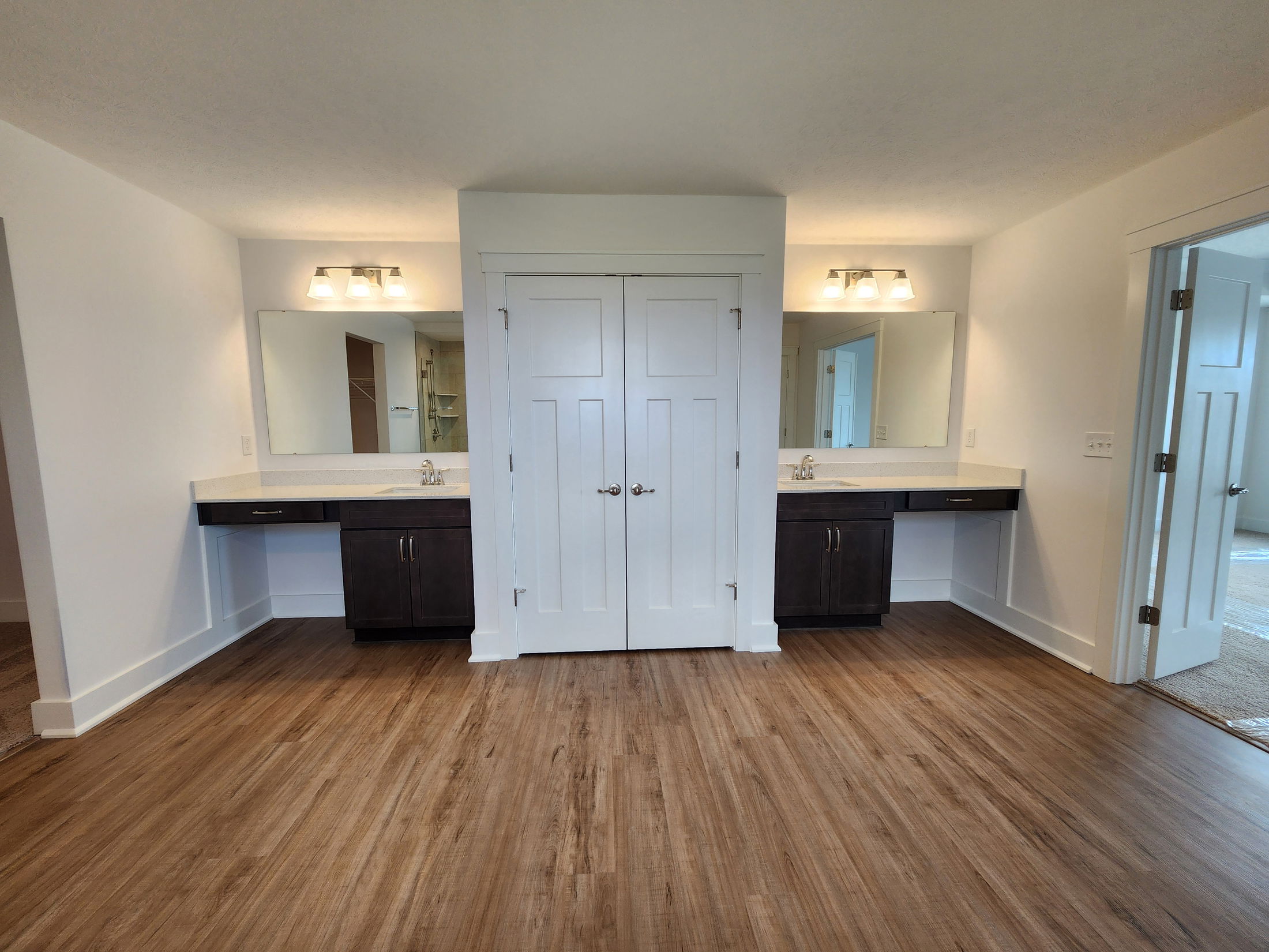 Modern bathroom with dual vanities, large mirrors, and wood flooring.