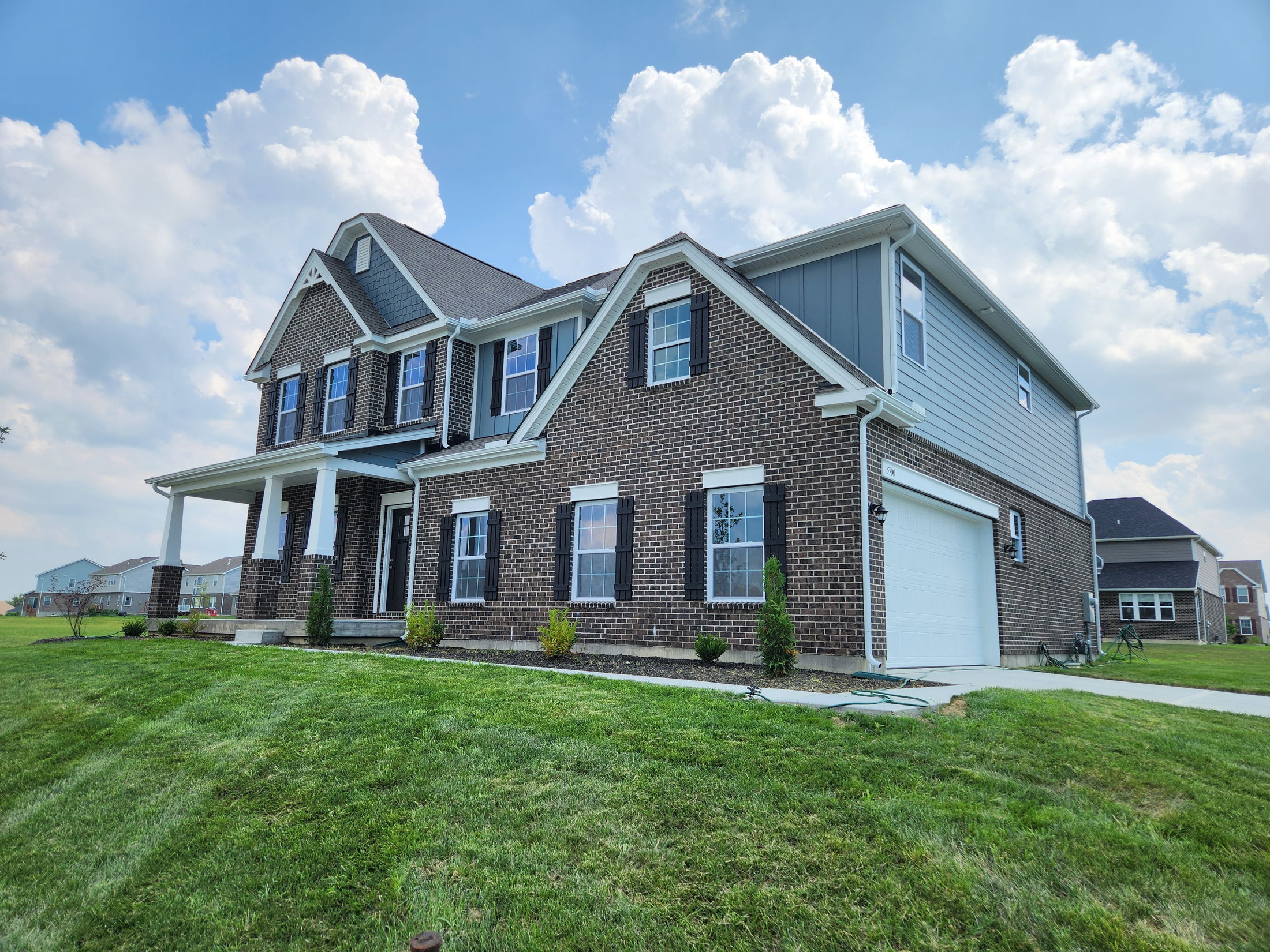 Two-story modern brick house with a manicured lawn under a blue sky with clouds.
