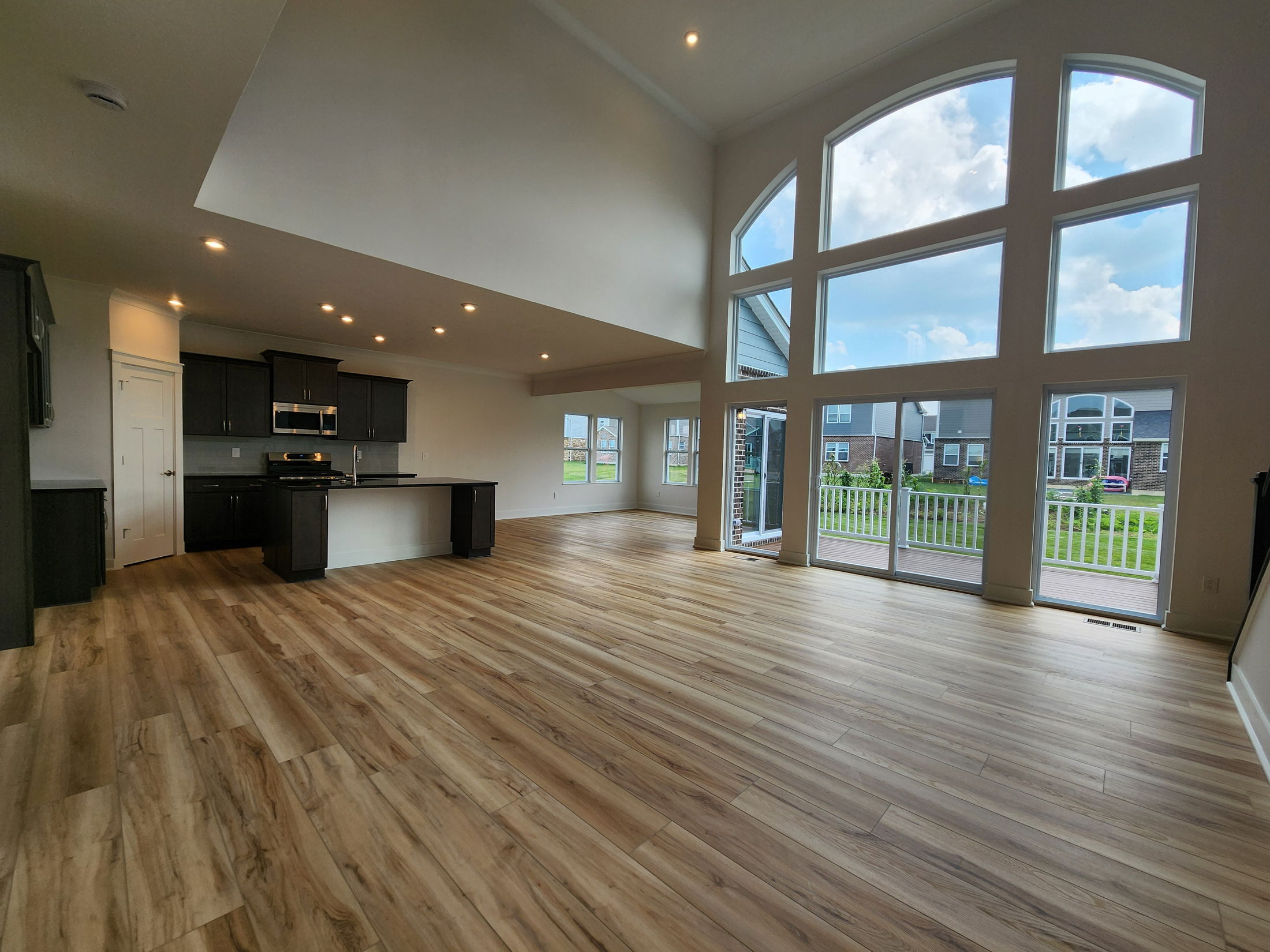 Spacious modern living room with large arched windows, hardwood floors, and an open kitchen design.