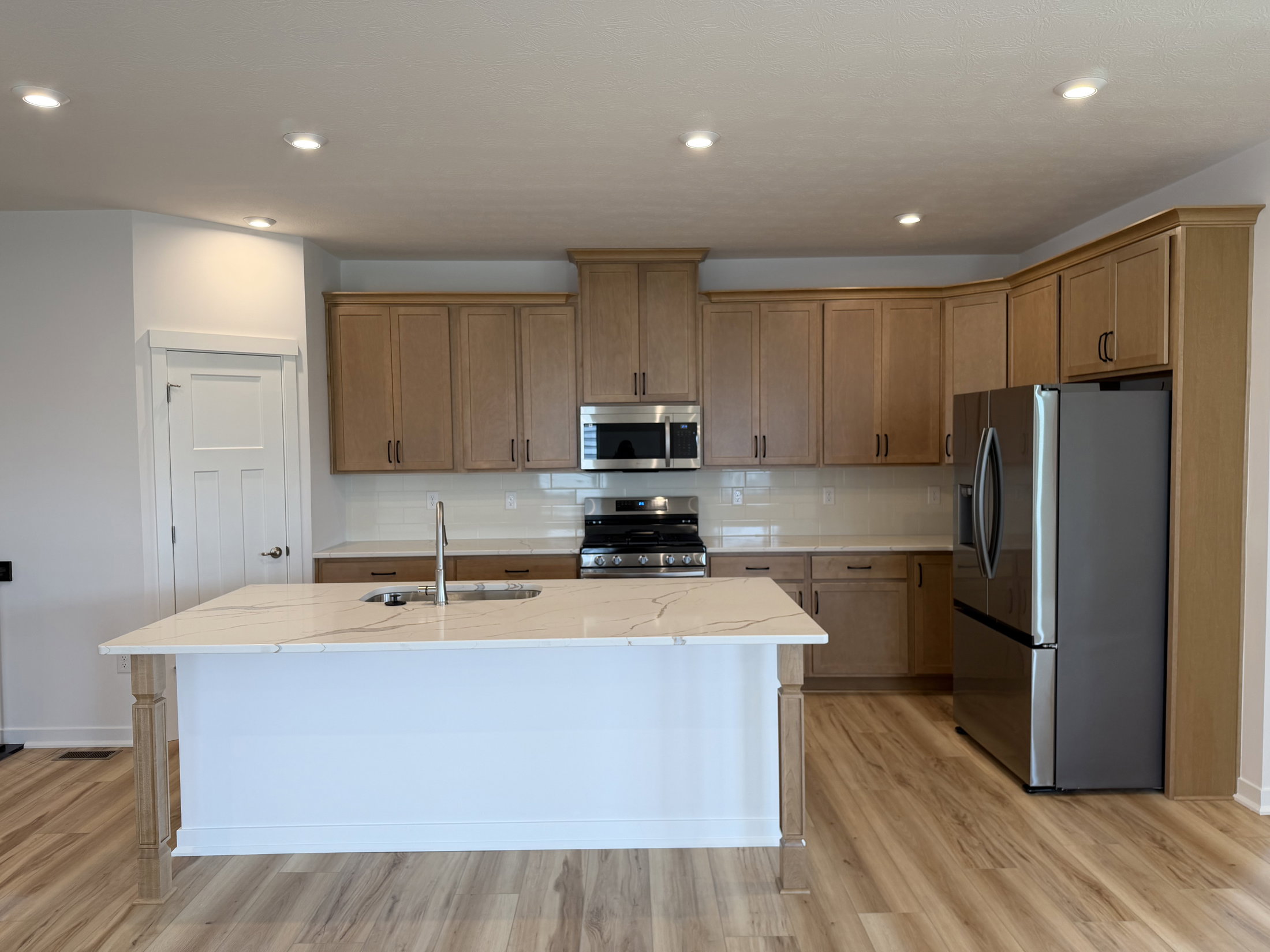 Modern kitchen featuring wooden cabinets, stainless steel appliances, and an island with a marble countertop.