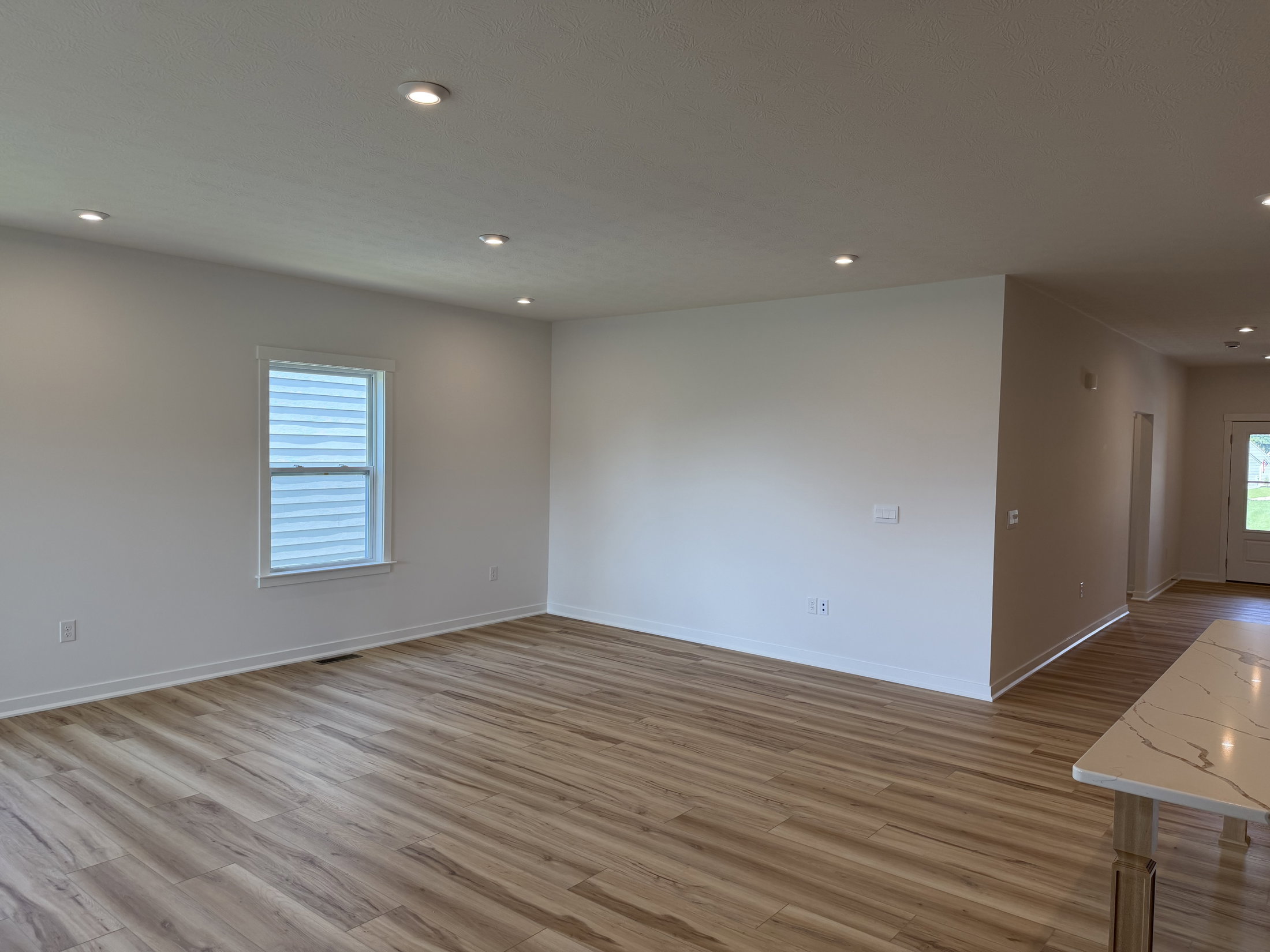 A spacious, empty room with wooden flooring, white walls, and recessed lighting.