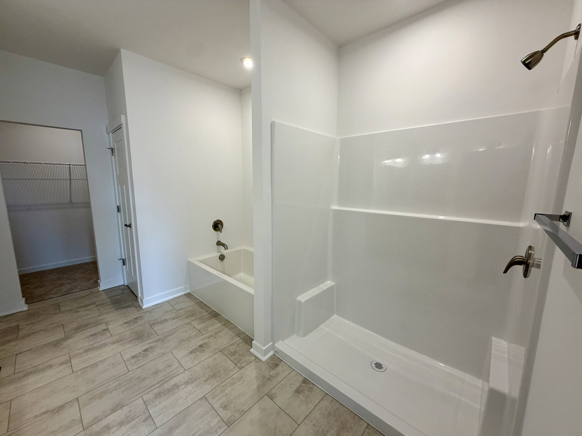 Modern bathroom featuring a shower stall and a separate bathtub with neutral-colored tiles.