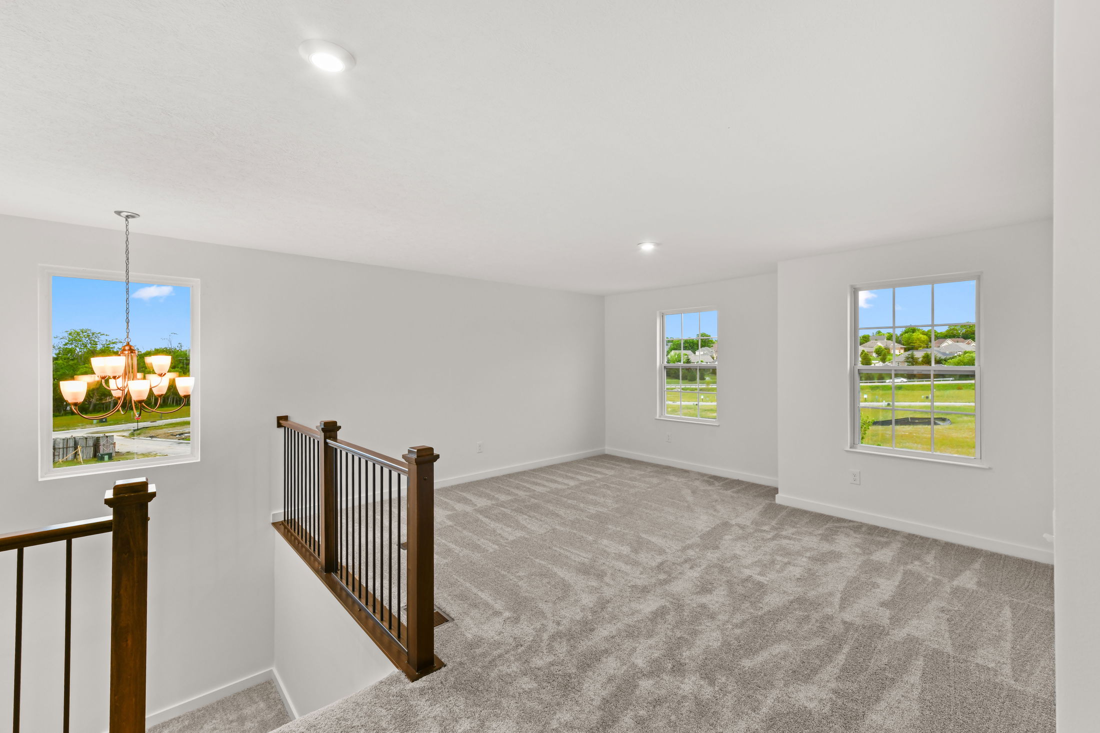 Bright, spacious carpeted room with large windows and a wooden banister overlooking a staircase.