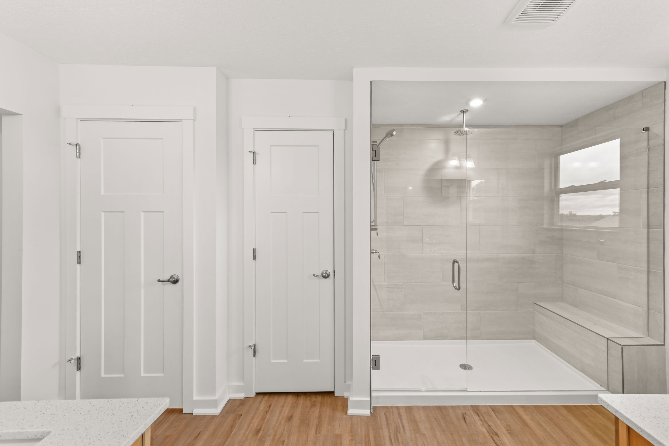 Modern bathroom with glass-enclosed shower, white panel doors, and light wood flooring.