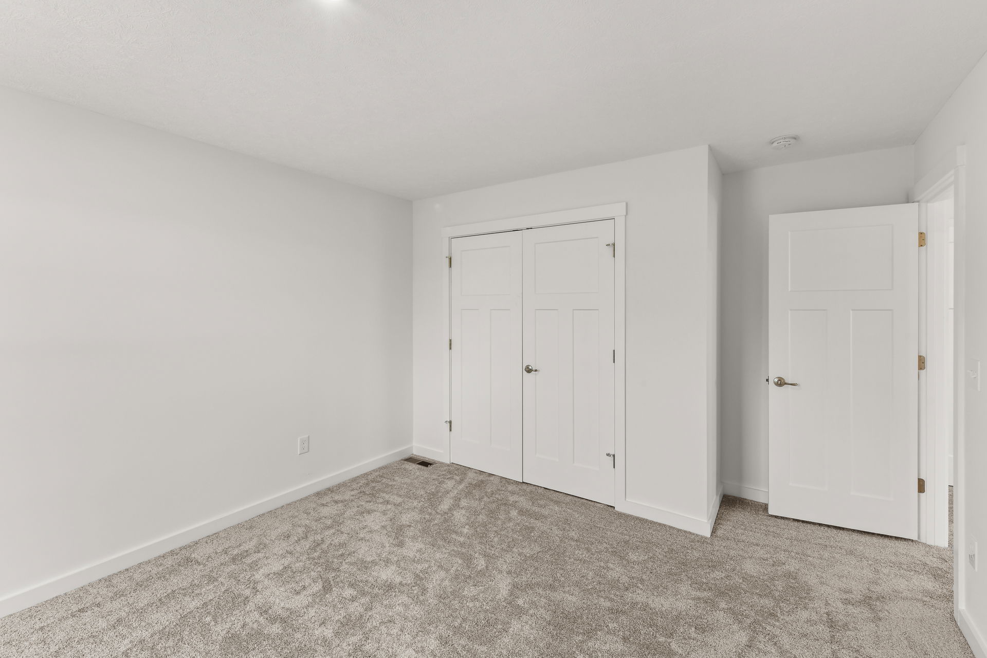 Empty white room with a closed closet, gray carpet flooring, and an open door.