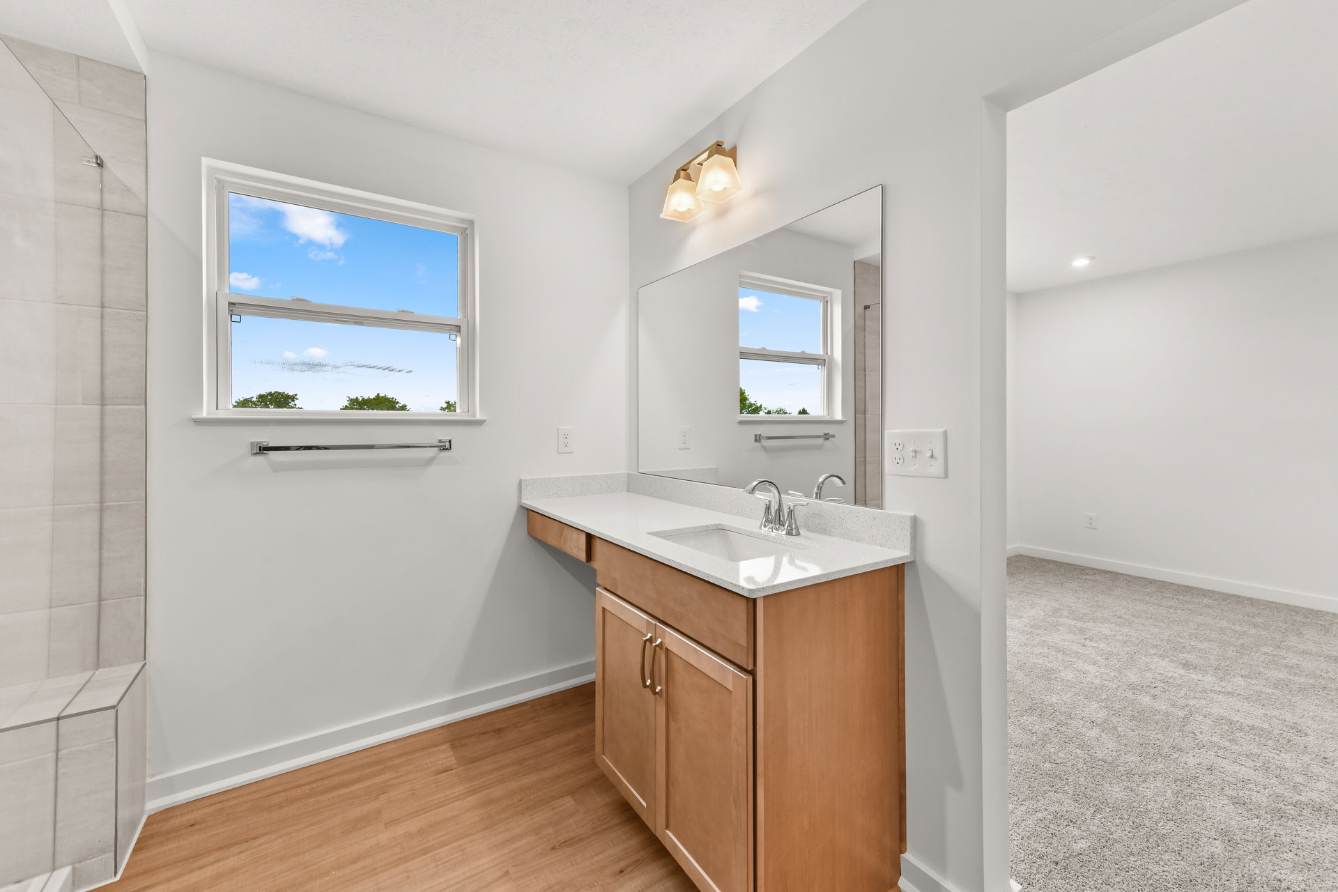 Modern bathroom interior with a wooden vanity, white countertop, large mirror, and a window with natural light.