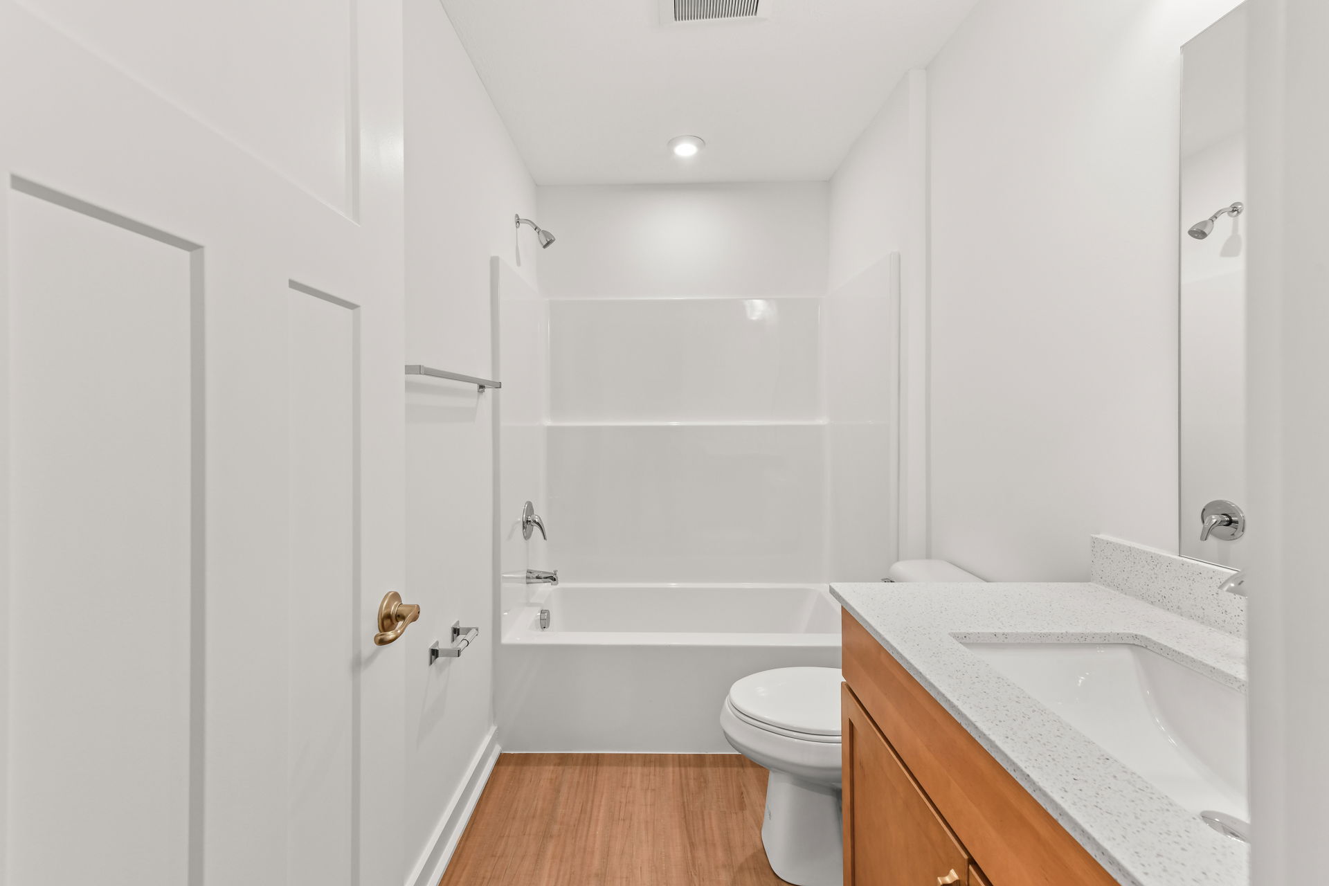 Modern white bathroom with wood flooring, featuring a bathtub, sink, and wooden cabinet.