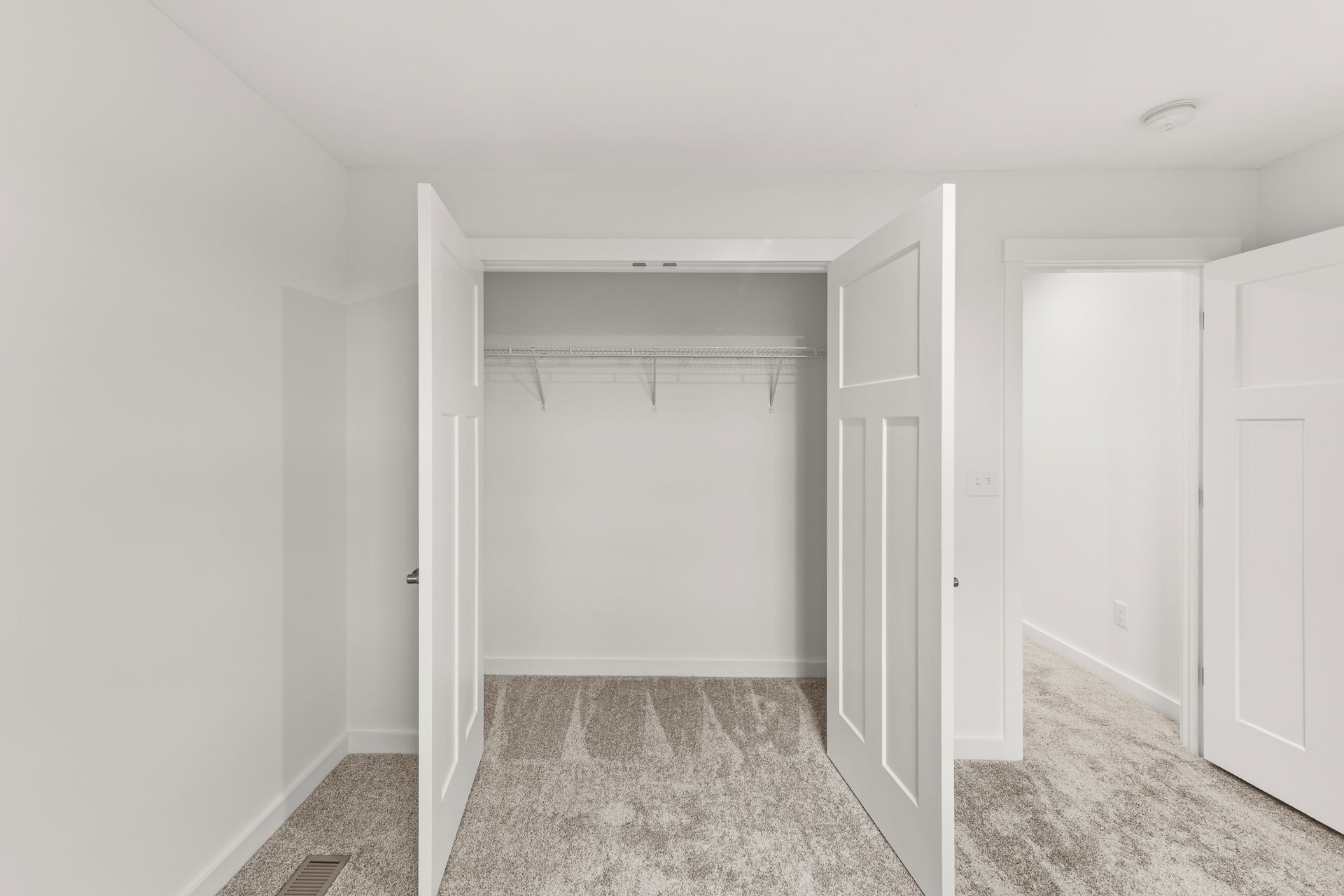 Empty white closet with open double doors and beige carpet flooring.