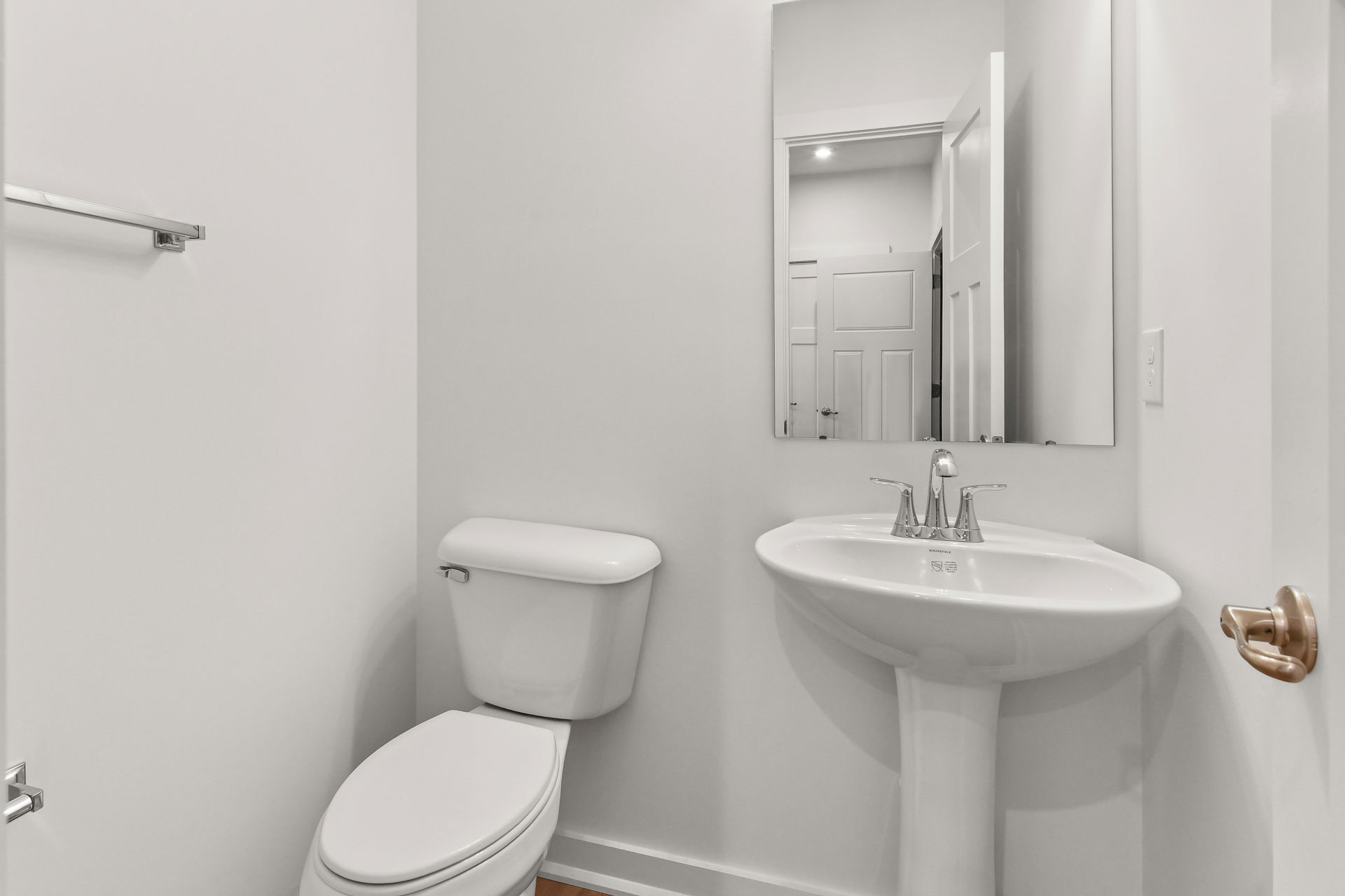 Minimalist modern bathroom with a white toilet, pedestal sink, and a large mirror on a gray wall.
