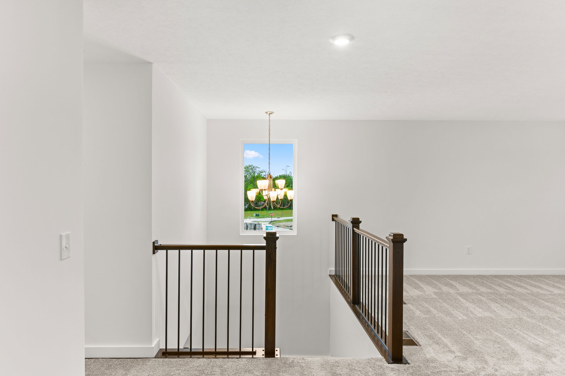 Modern home interior with a carpeted staircase and elegant chandelier, featuring a window view of greenery.