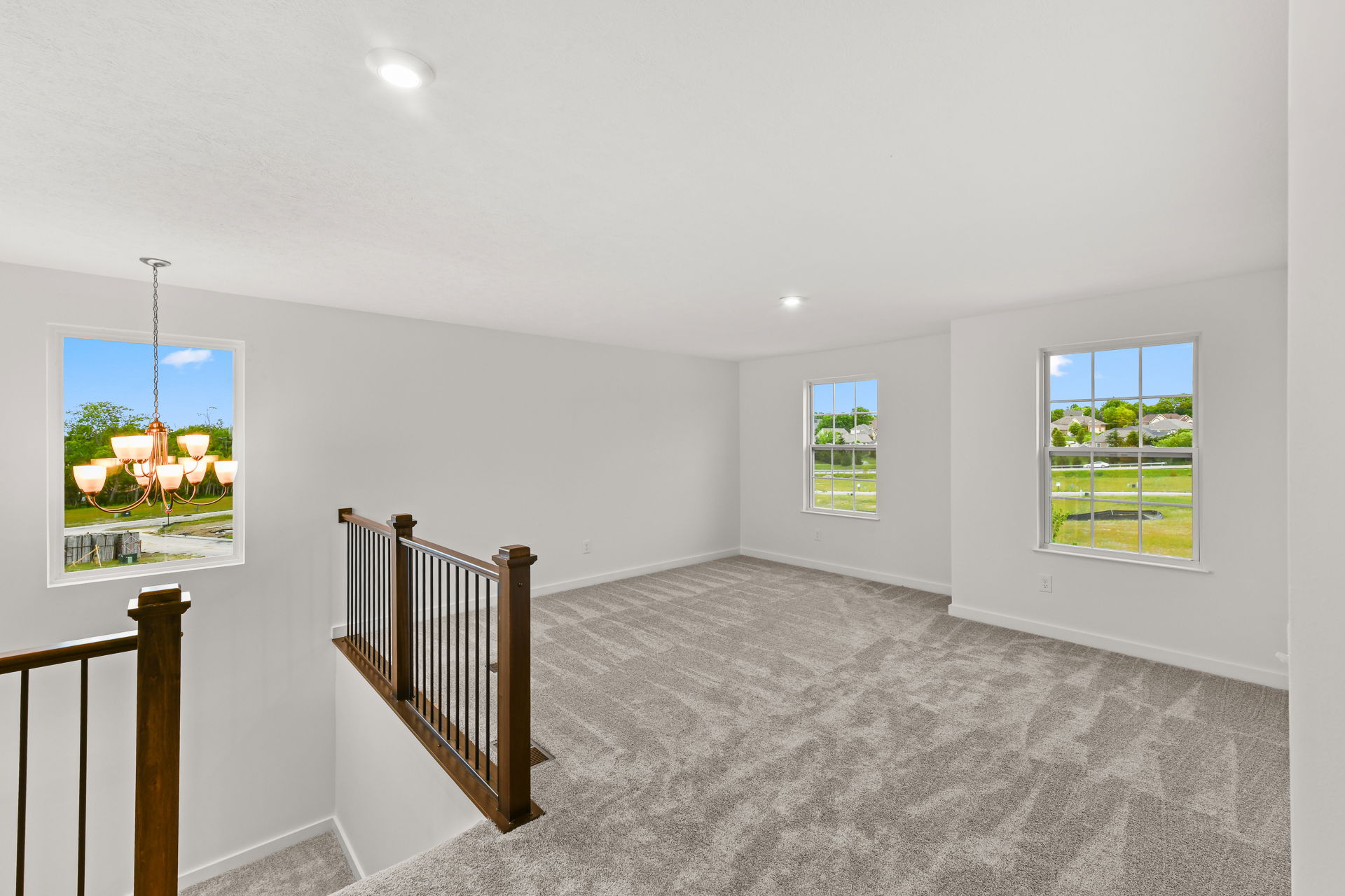 Spacious and well-lit upstairs area with large windows, carpeted flooring, and wooden railing overlooking a scenic view.