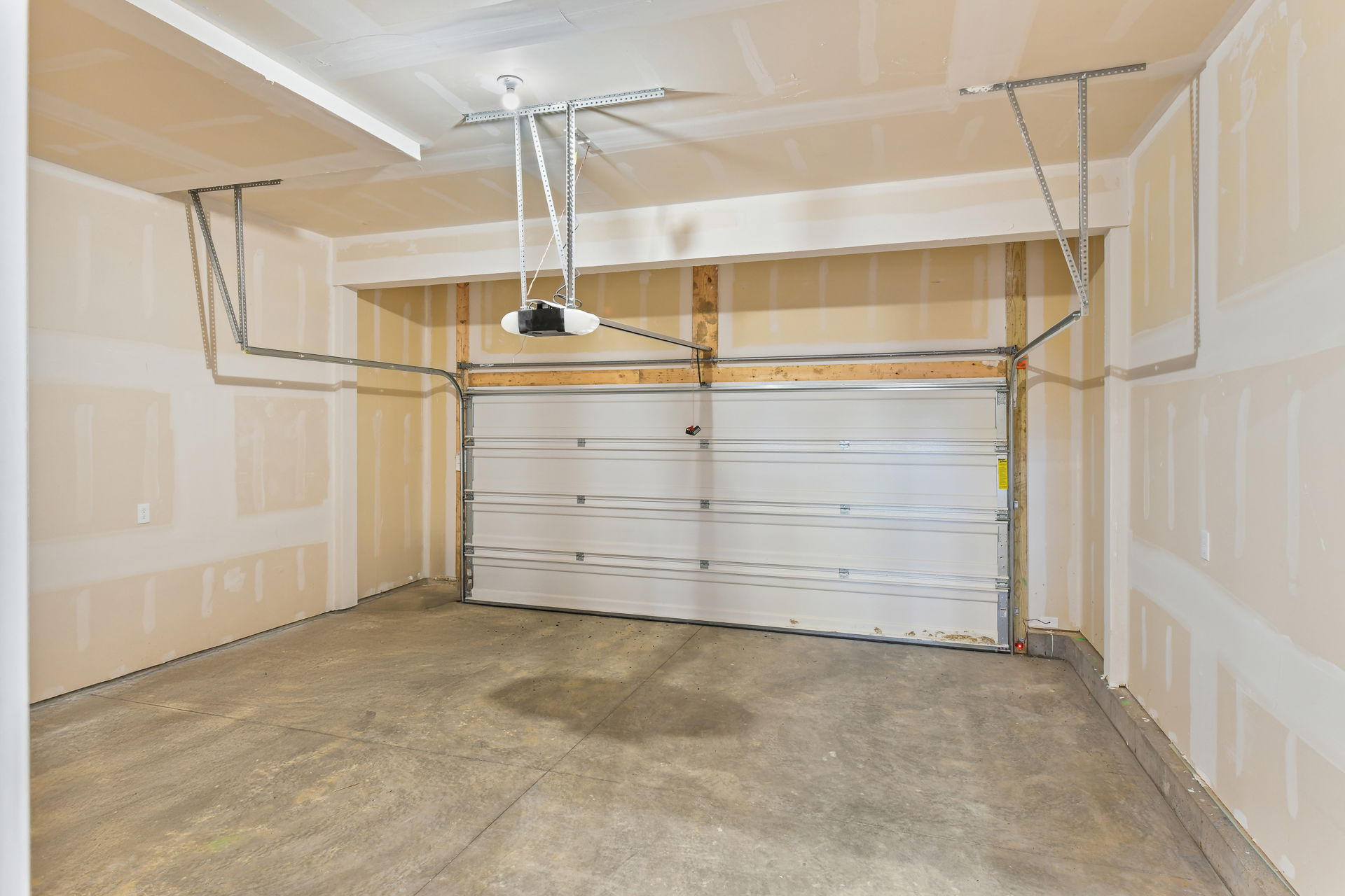 Empty residential garage with closed sectional garage door and ceiling-mounted opener mechanism.