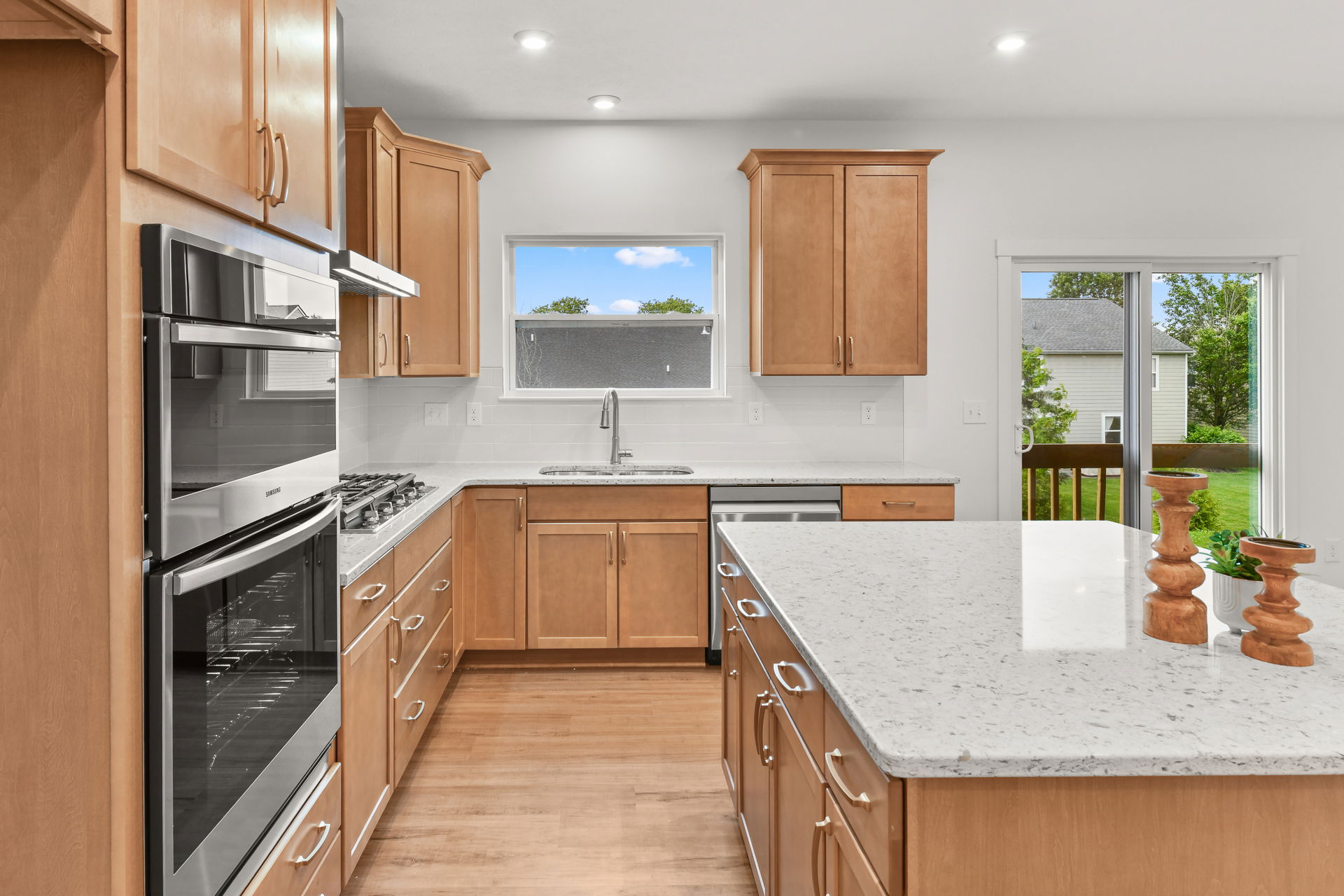 Modern kitchen with light wood cabinets, stainless steel appliances, and a large marble island.