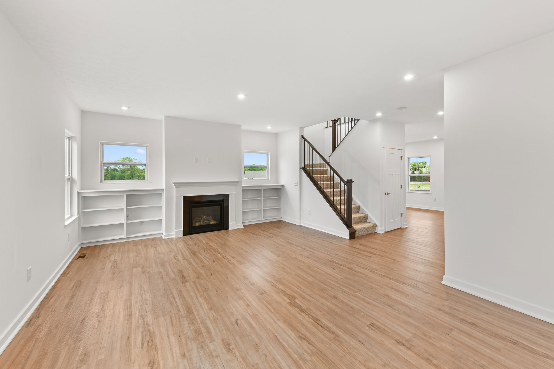 Modern living room with hardwood floors, a fireplace, built-in shelves, and a staircase leading upstairs.
