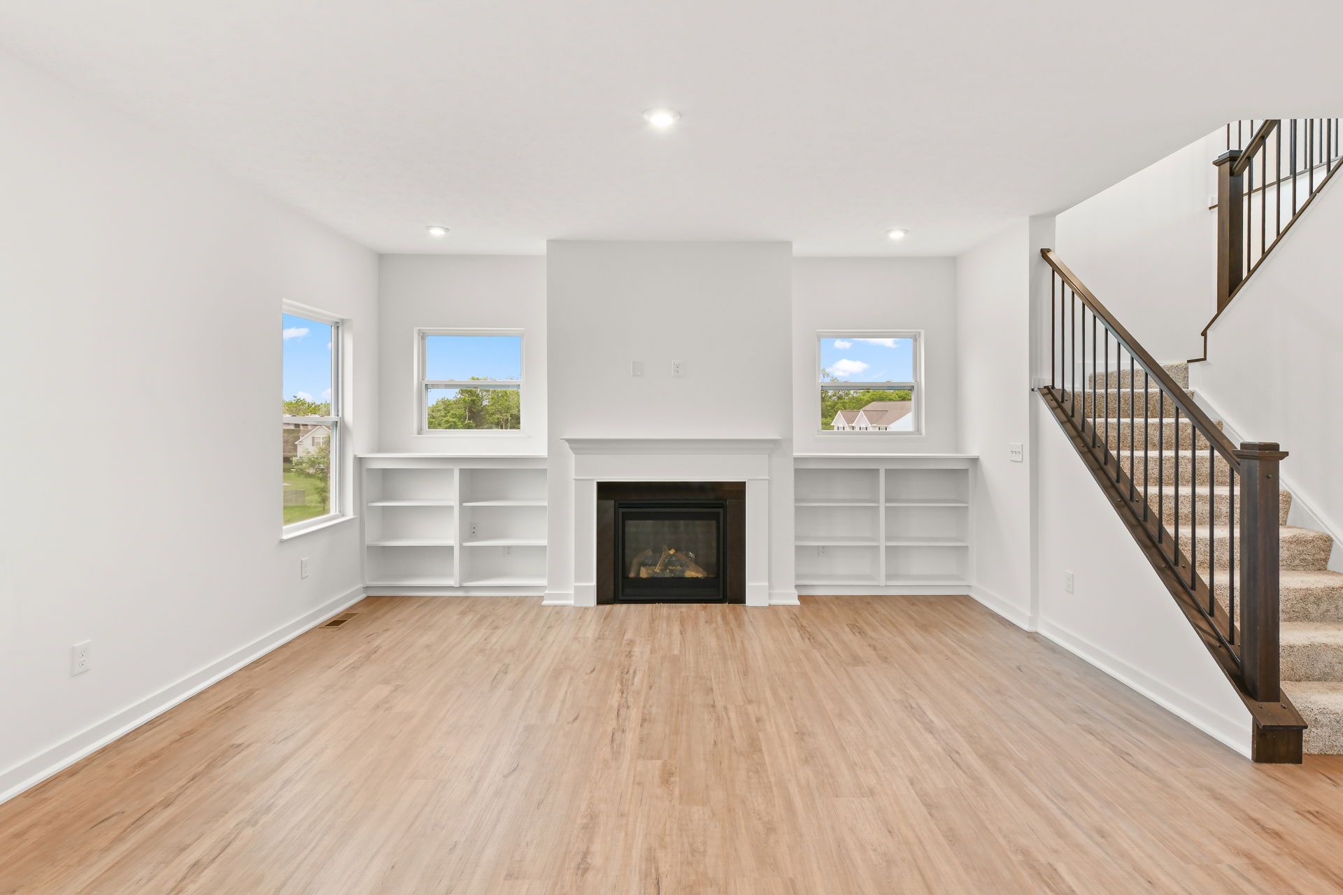 Modern living room with hardwood floors, a central fireplace flanked by built-in shelves, and a staircase leading upstairs.