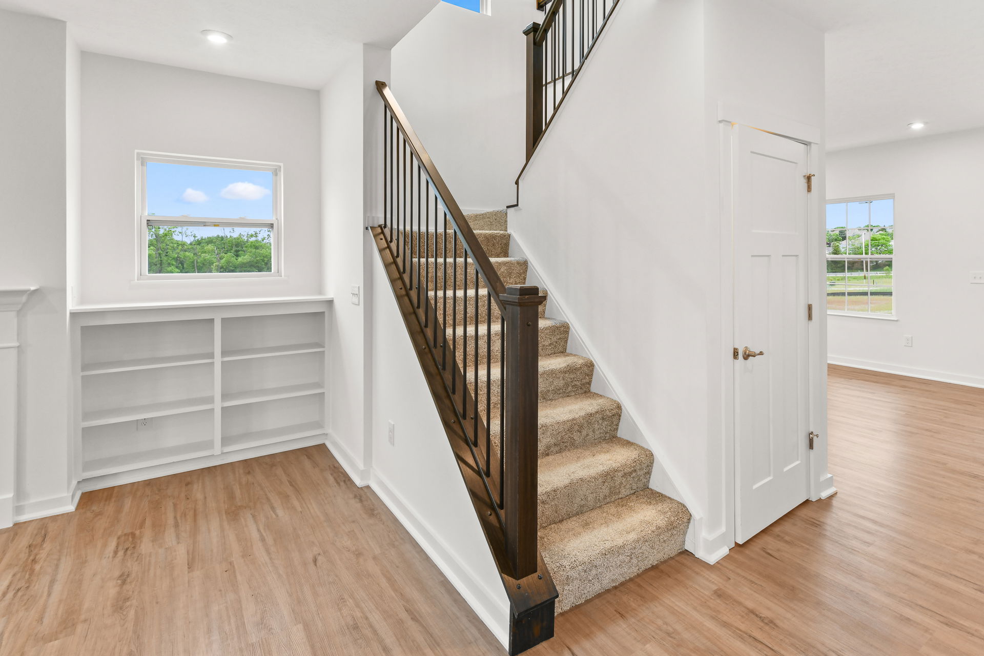 Modern home interior with carpeted staircase, wooden railing, built-in bookshelf, and hardwood floors.
