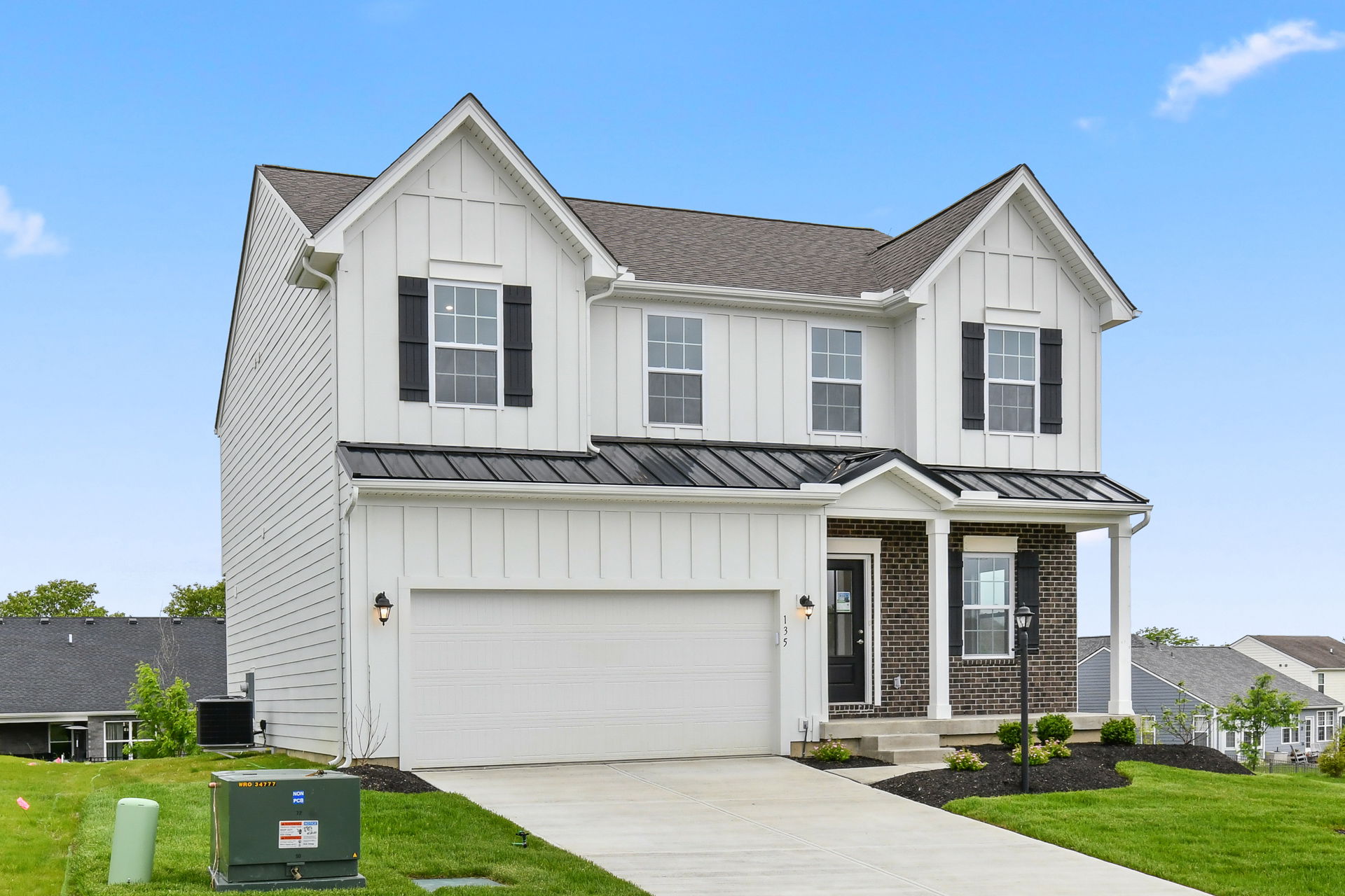 Two-story modern farmhouse exterior with white siding, black shutters, and a spacious garage against a clear blue sky.