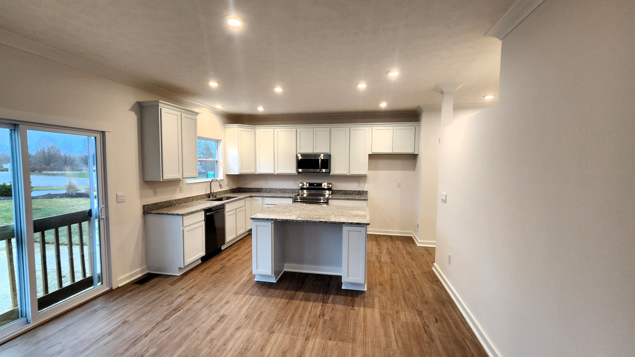 Modern kitchen with white cabinets, granite countertops, stainless steel appliances, and hardwood flooring.