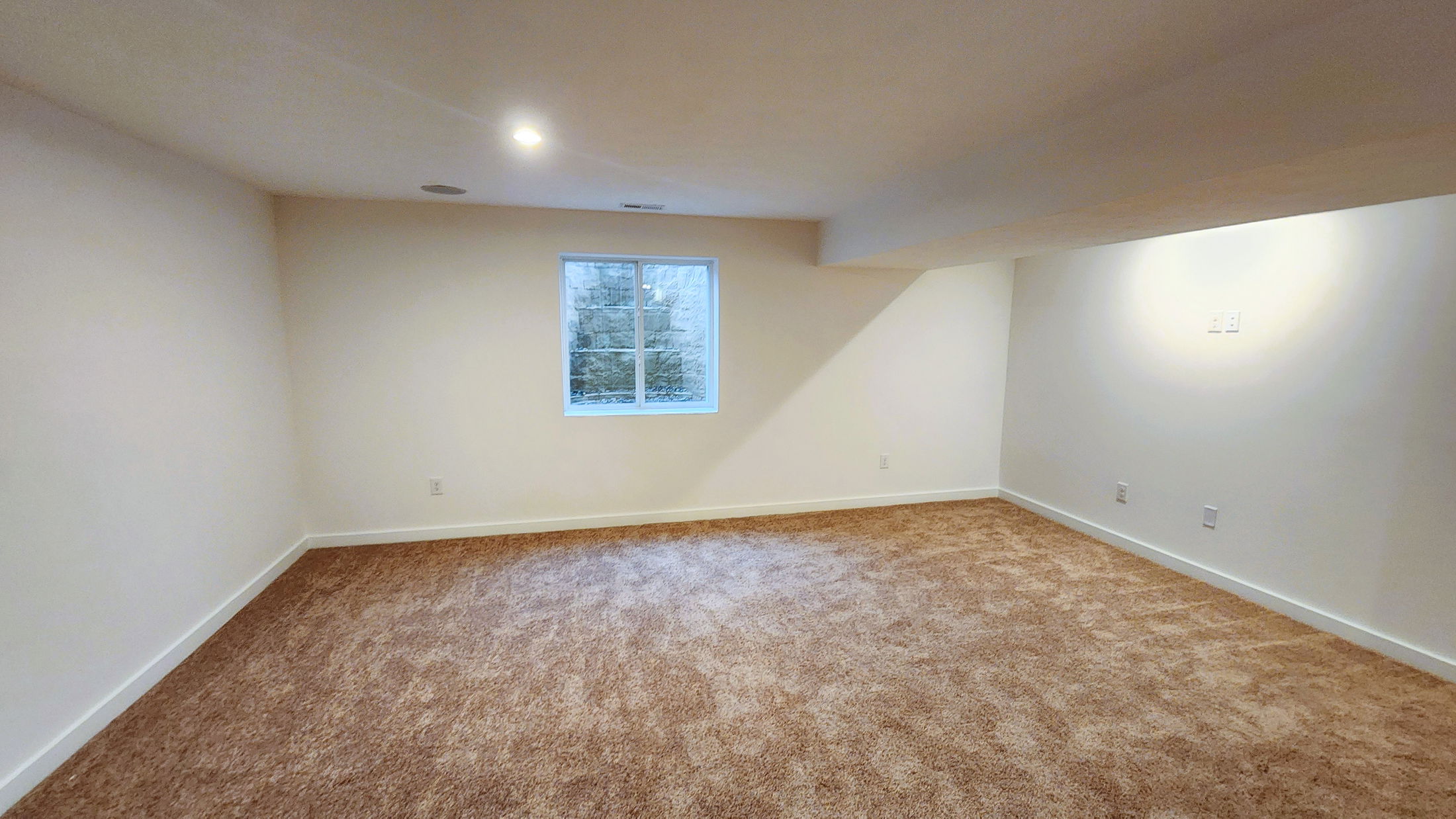 Spacious, empty room with beige carpet and a window allowing natural light in, ideal for a home renovation or decoration project.