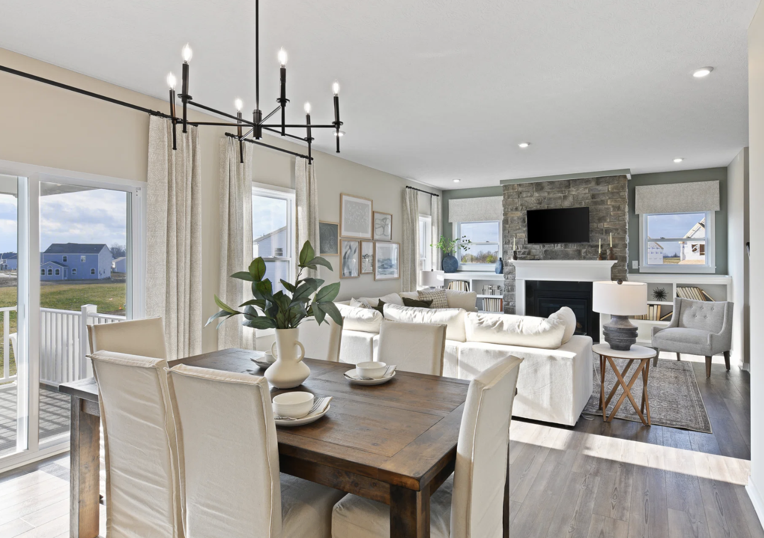 A modern living and dining area featuring a wooden dining table set for four, a cozy sofa, and a stone fireplace with large windows letting in natural light.