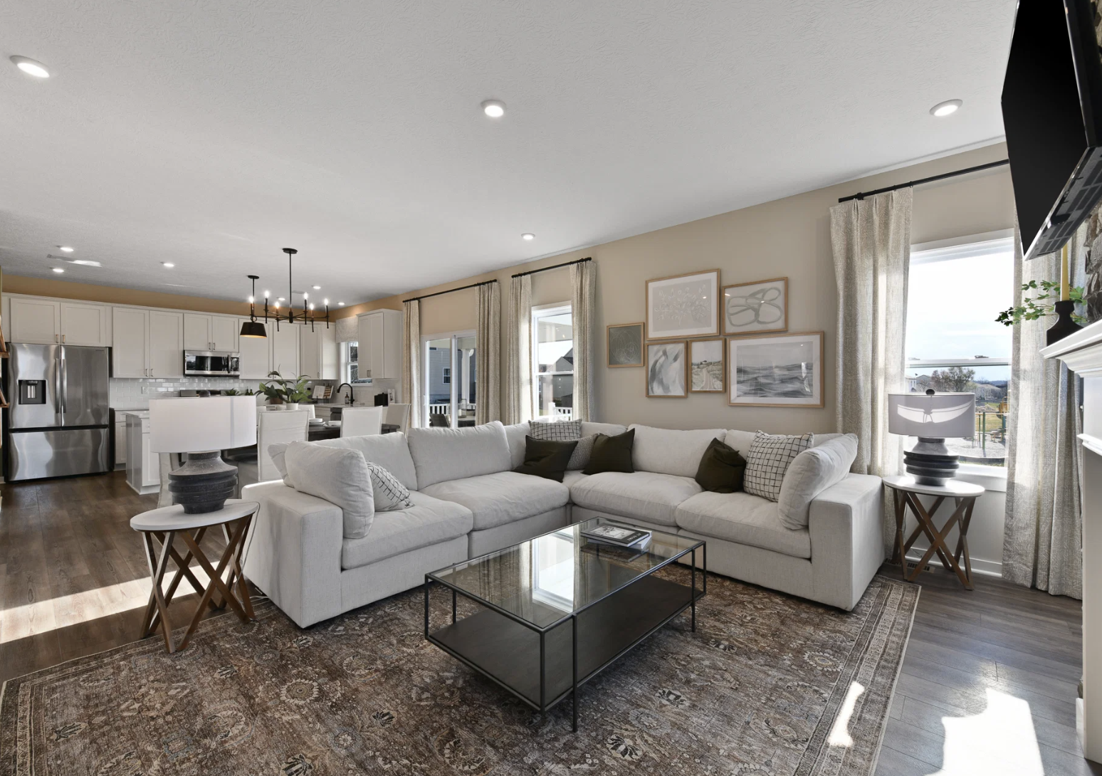 A spacious, modern living room featuring a large beige sectional sofa, a glass coffee table, and decorative wall art.