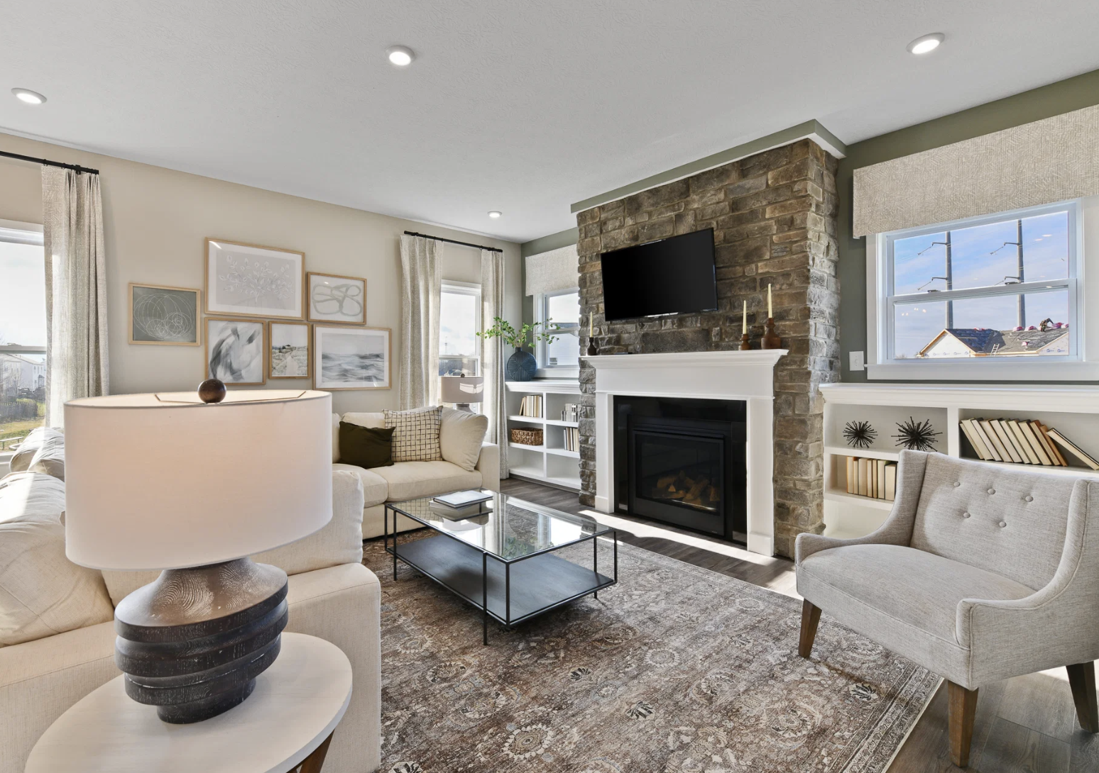 Spacious living room featuring a stone fireplace, modern furniture, and large windows with natural light.