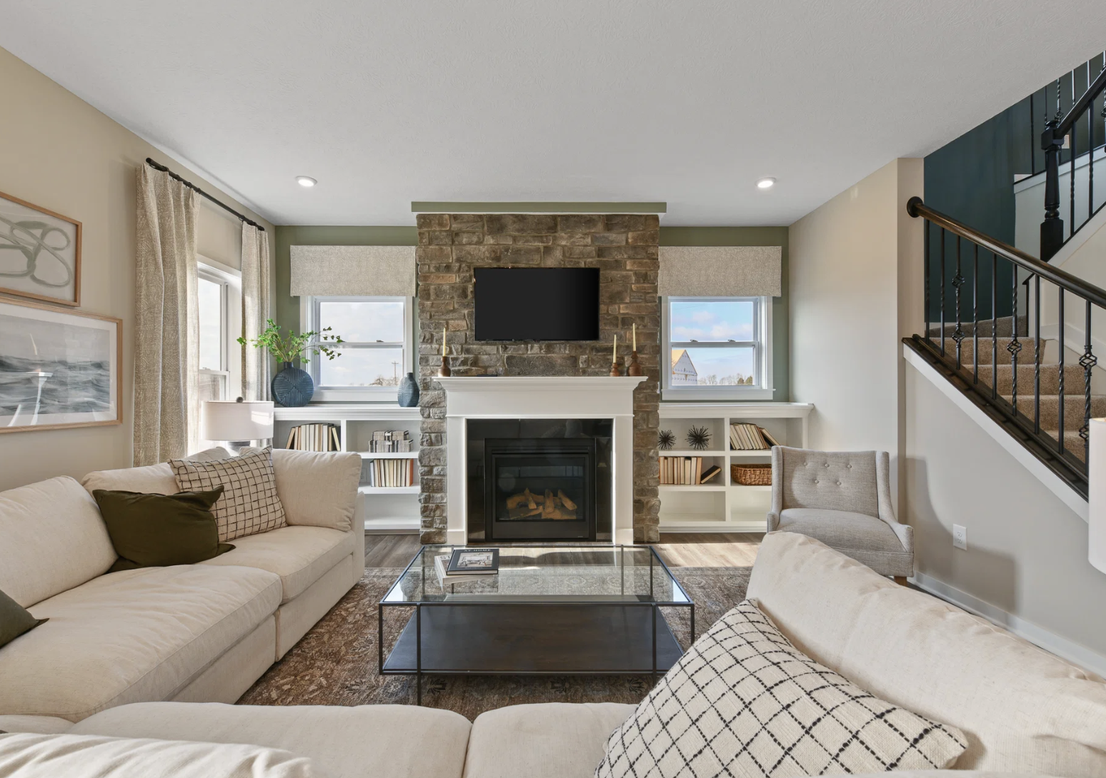Spacious living room featuring a stone fireplace, large windows with window treatments, and a sectional sofa.