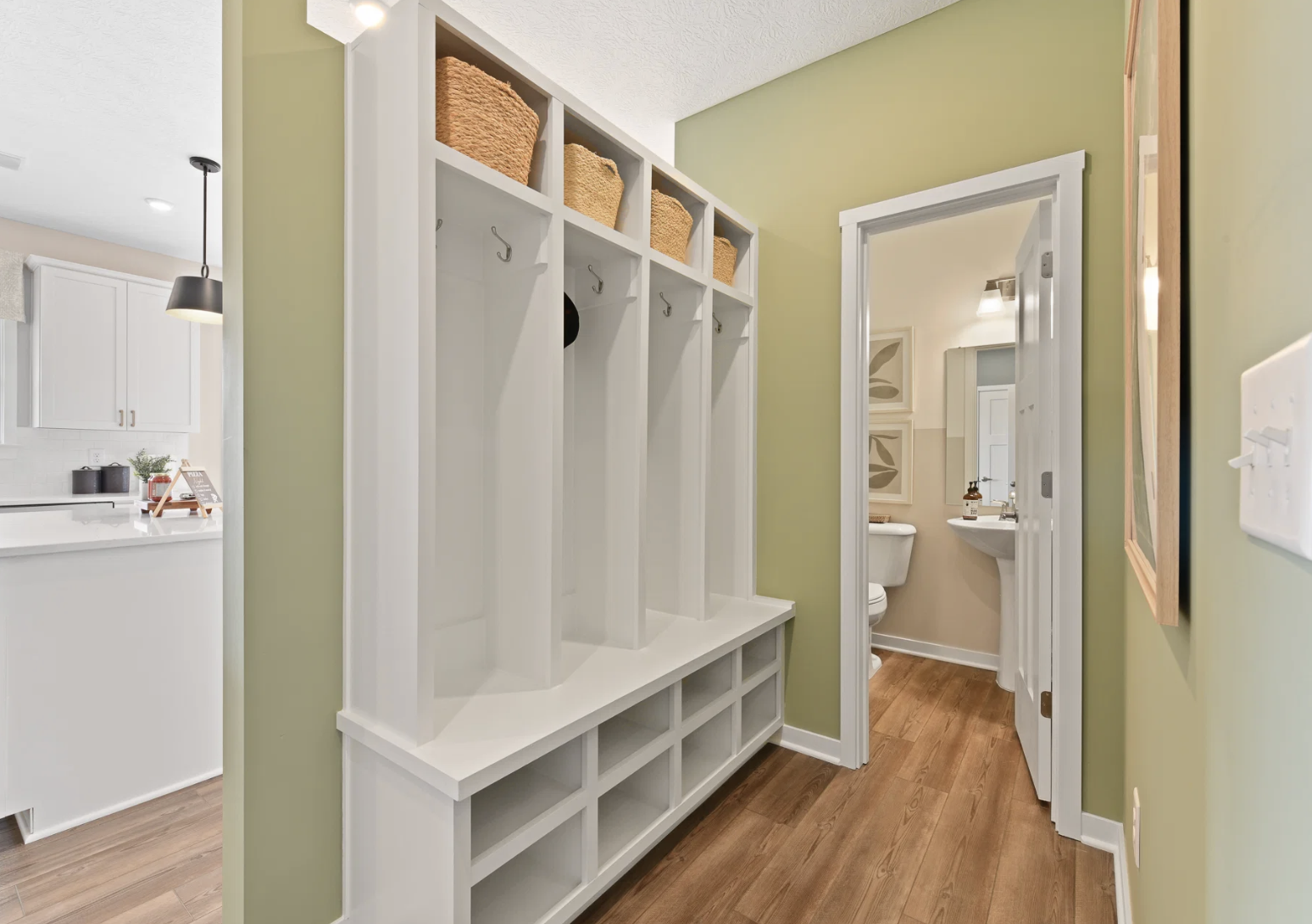 A modern entryway features a white wall-mounted coat rack with baskets and a small adjoining bathroom doorway.