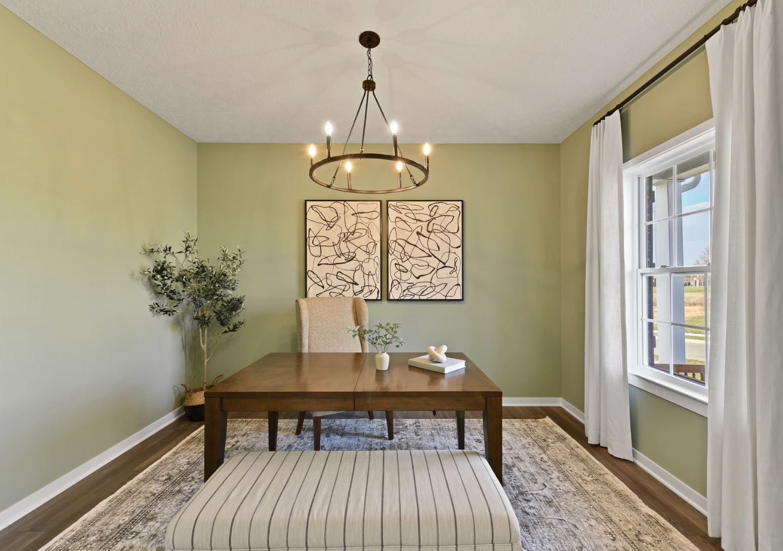 A modern dining area featuring a wooden table, a decorative bench, light green walls, and two framed wall art pieces.