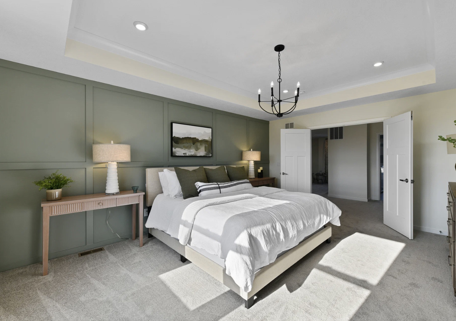 Spacious bedroom with a green accent wall, a bed with white bedding, bedside tables with lamps, and a chandelier.