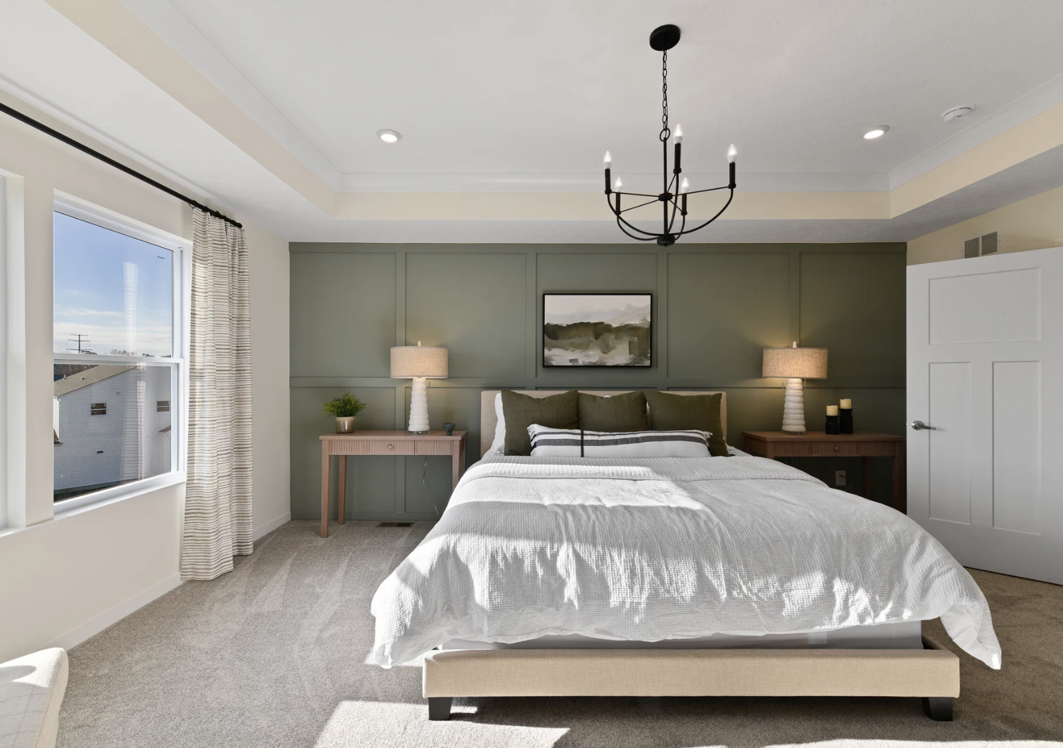 A cozy bedroom featuring a large bed, two bedside lamps, a chandelier, and green accent walls.