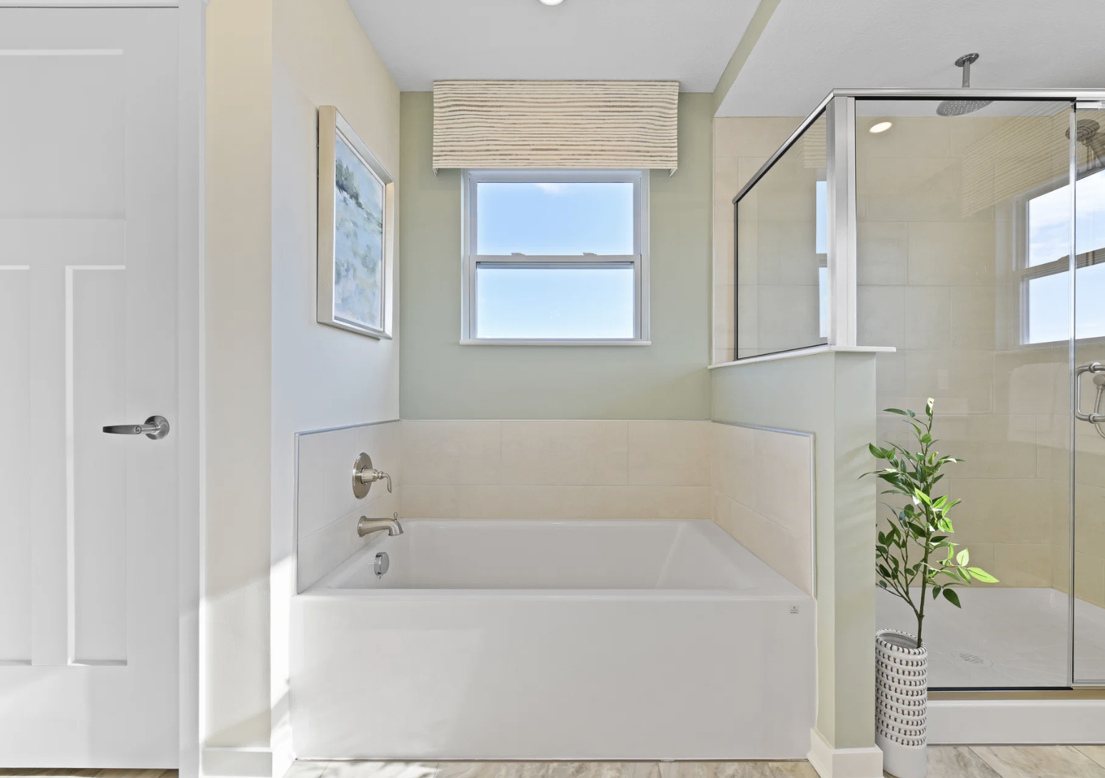 A modern bathroom featuring a white bathtub, a glass shower, and a window with natural light.