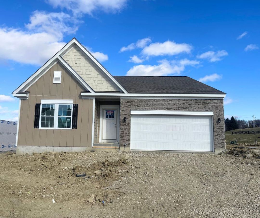 Front view of a new construction house featuring brick and siding with a garage and blue sky in the background.
