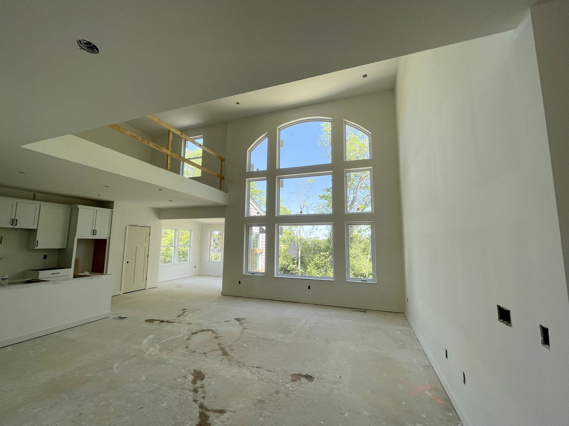 Spacious, modern living room with large arched windows and an upper balcony under construction.