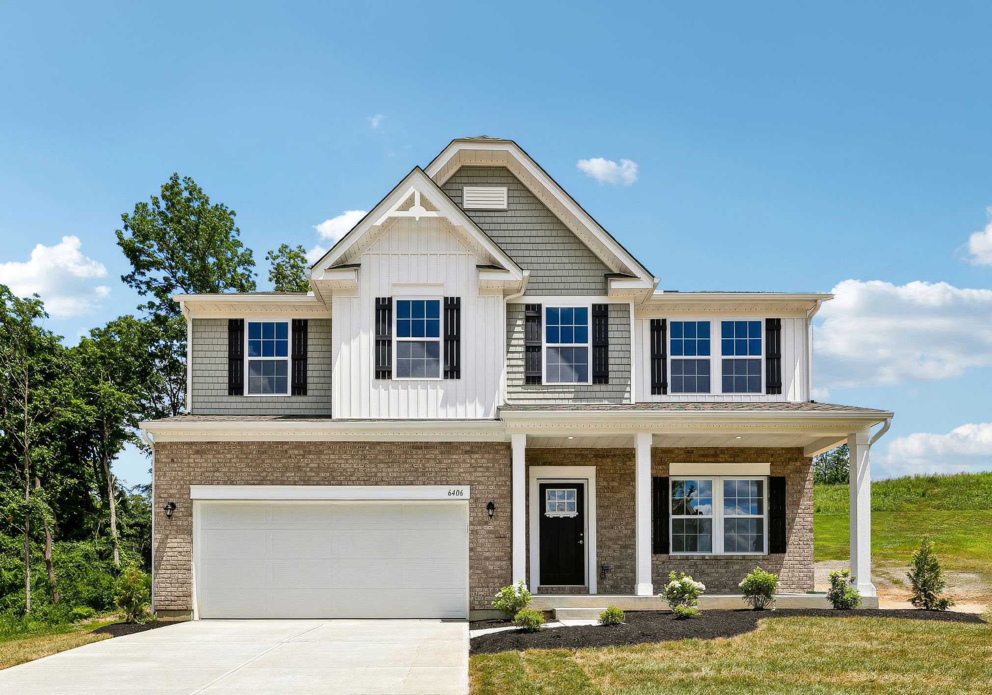 Two-story house with a brick façade, white shutters, and a grassy yard under a clear blue sky.