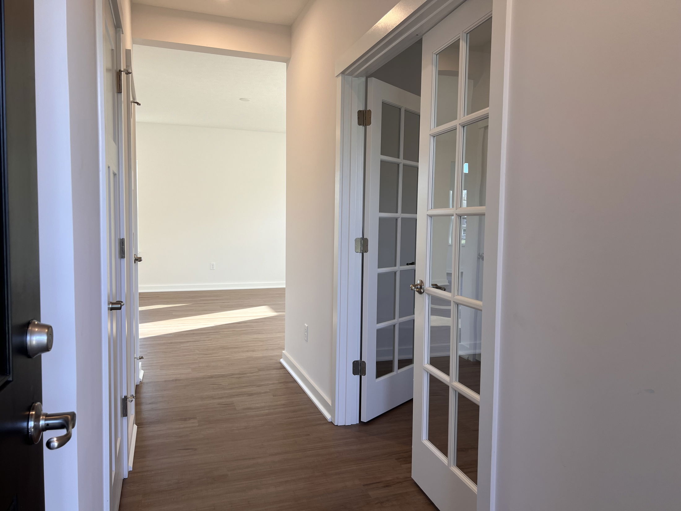 Bright hallway with wood flooring and open glass-paneled French doors in a modern home.