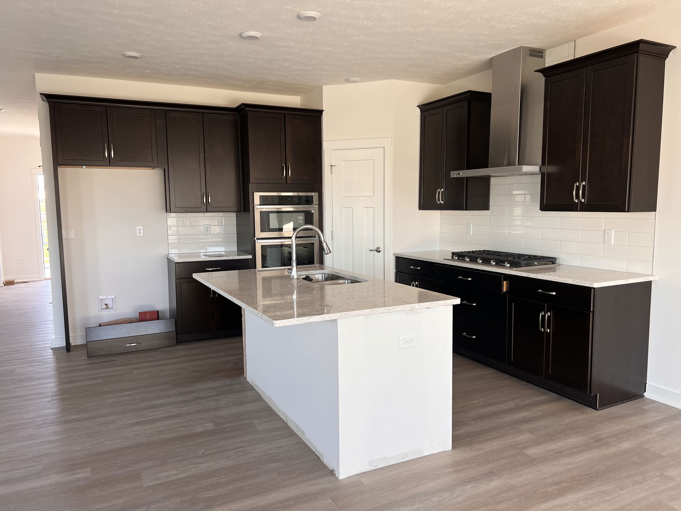 Modern kitchen with dark wood cabinets, stainless steel appliances, and a central island on hardwood floors.