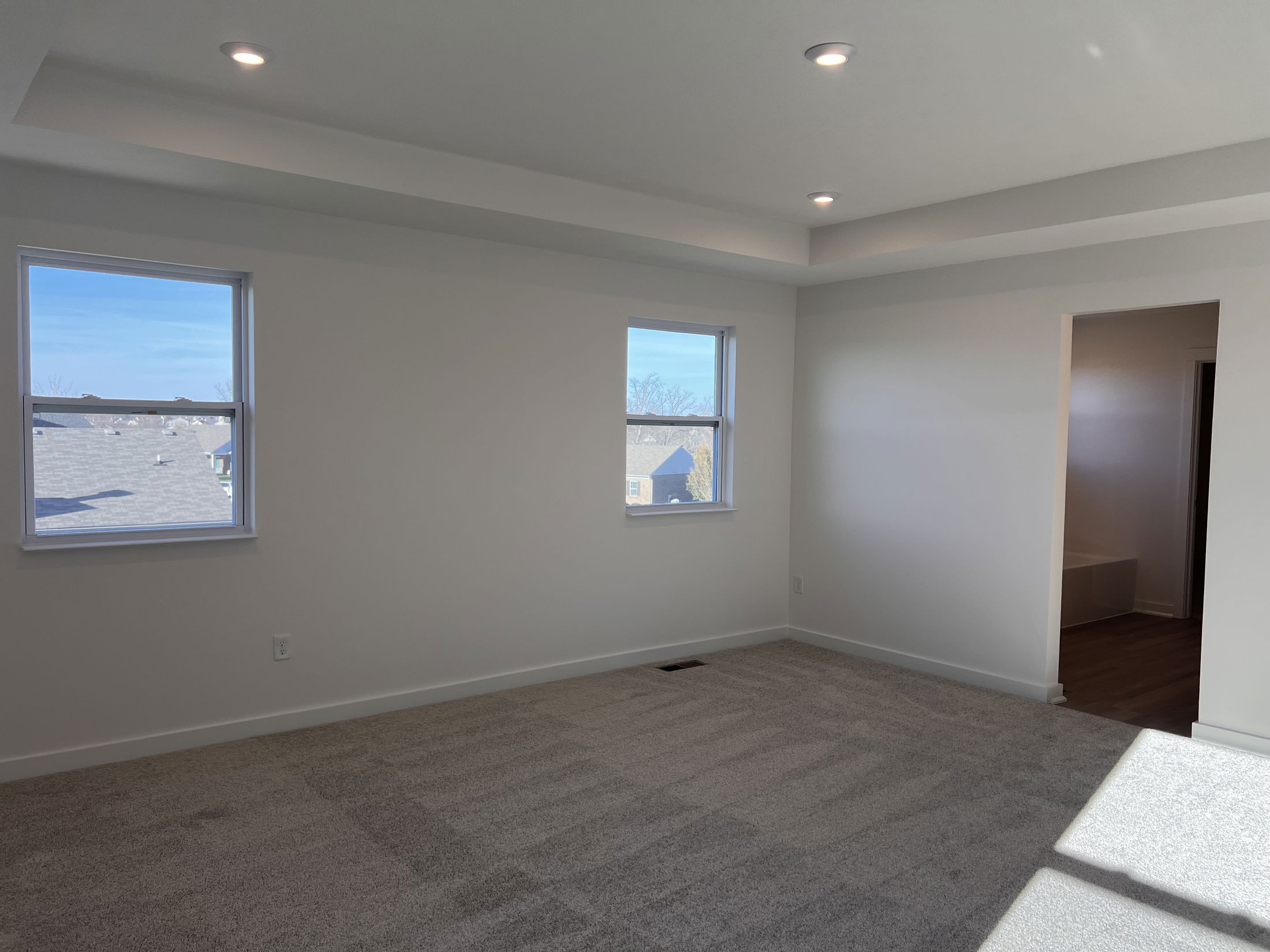Empty, well-lit room with beige carpet and two windows, showcasing a clean, modern interior design.