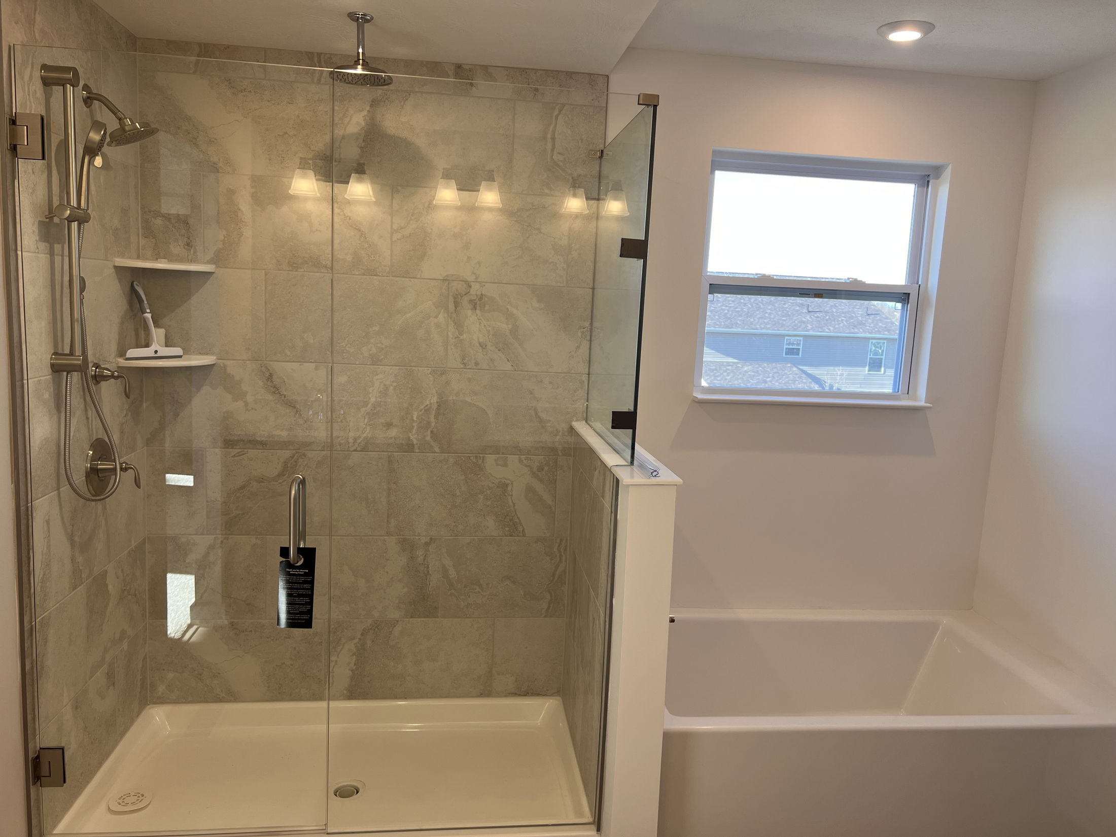 Modern bathroom featuring a spacious glass-enclosed shower with dual showerheads, adjacent to a built-in bathtub and large window for natural light.